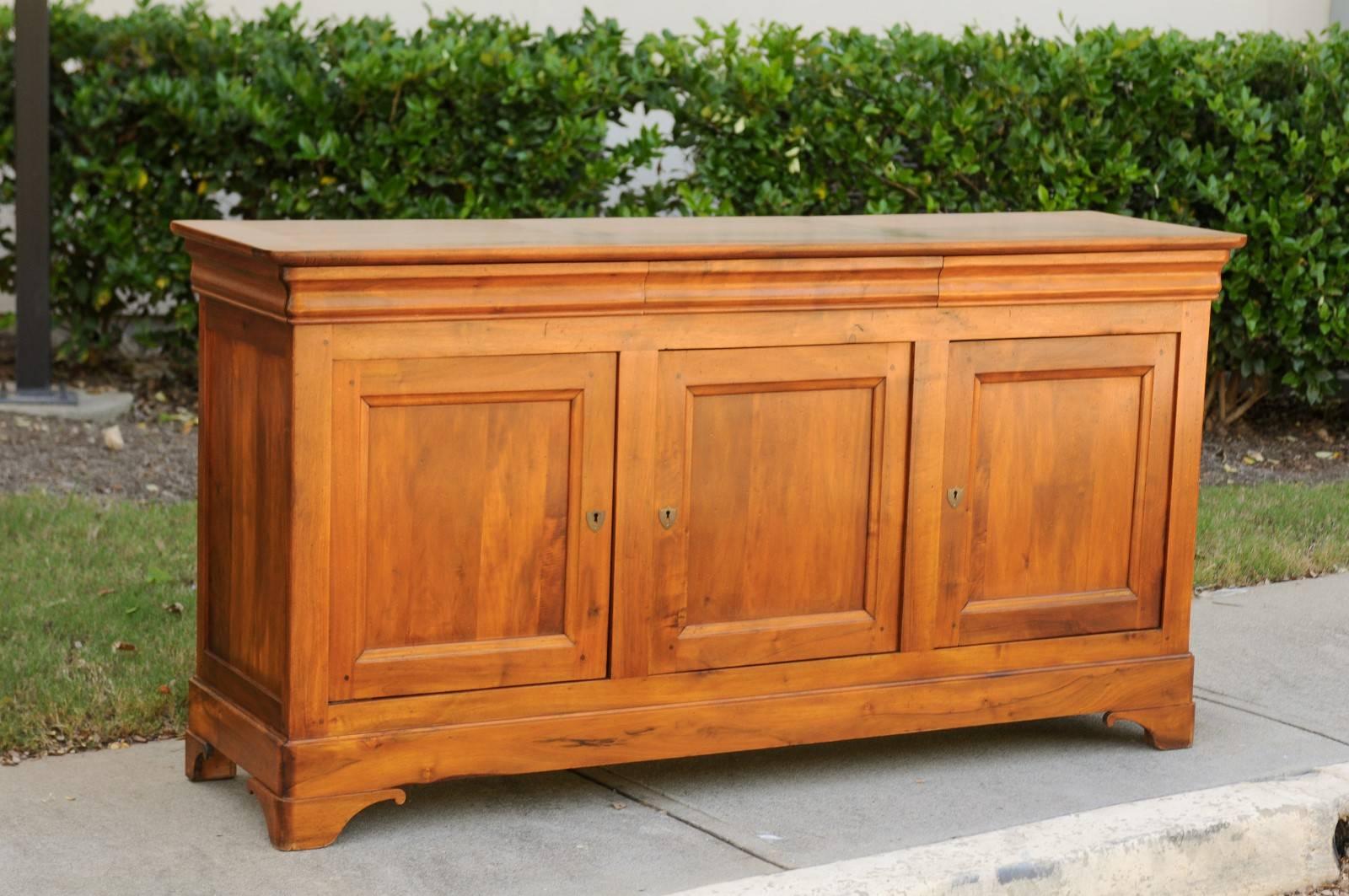 A French wooden enfilade with three drawers over three doors from the early 20th century. This French long buffet features a rectangular planked top over three dovetailed drawers, ingeniously hidden in the apron. Three doors with recessed panels