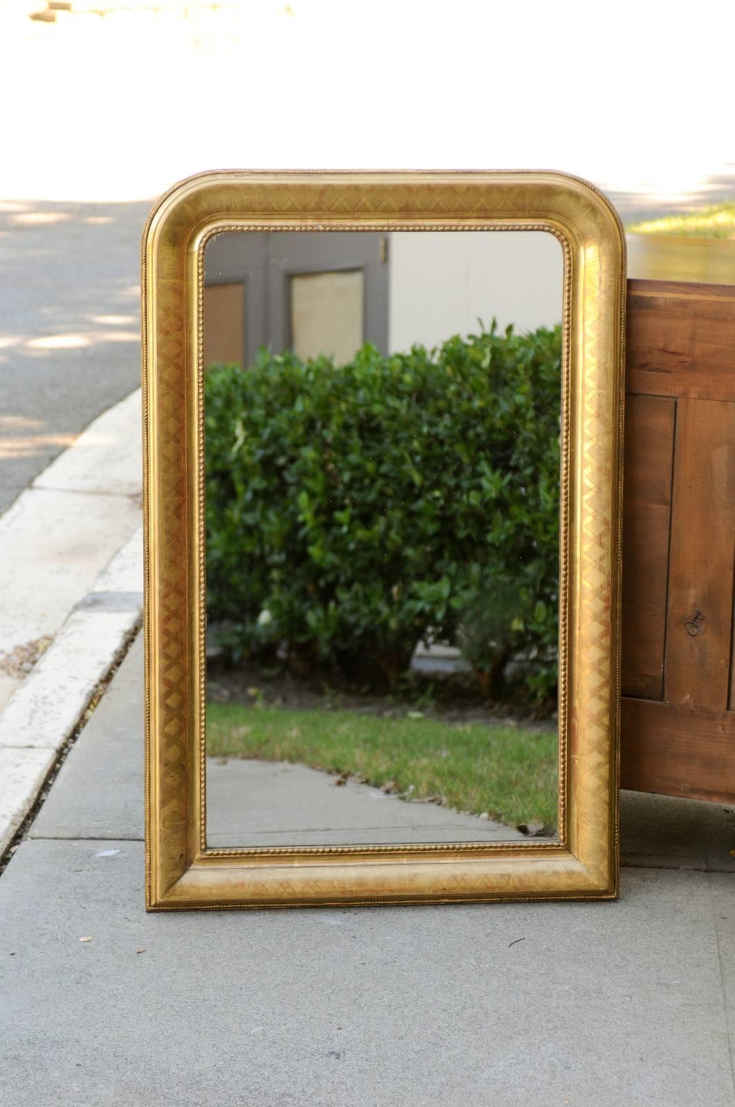 A French Louis-Philippe style giltwood mirror from the turn of the century. Born in the 1890s - 1900s during the Belle-Epoque era, this French wall mirror features the traditional Louis-Philippe Silhouette, with its vertical rectangular shape marked