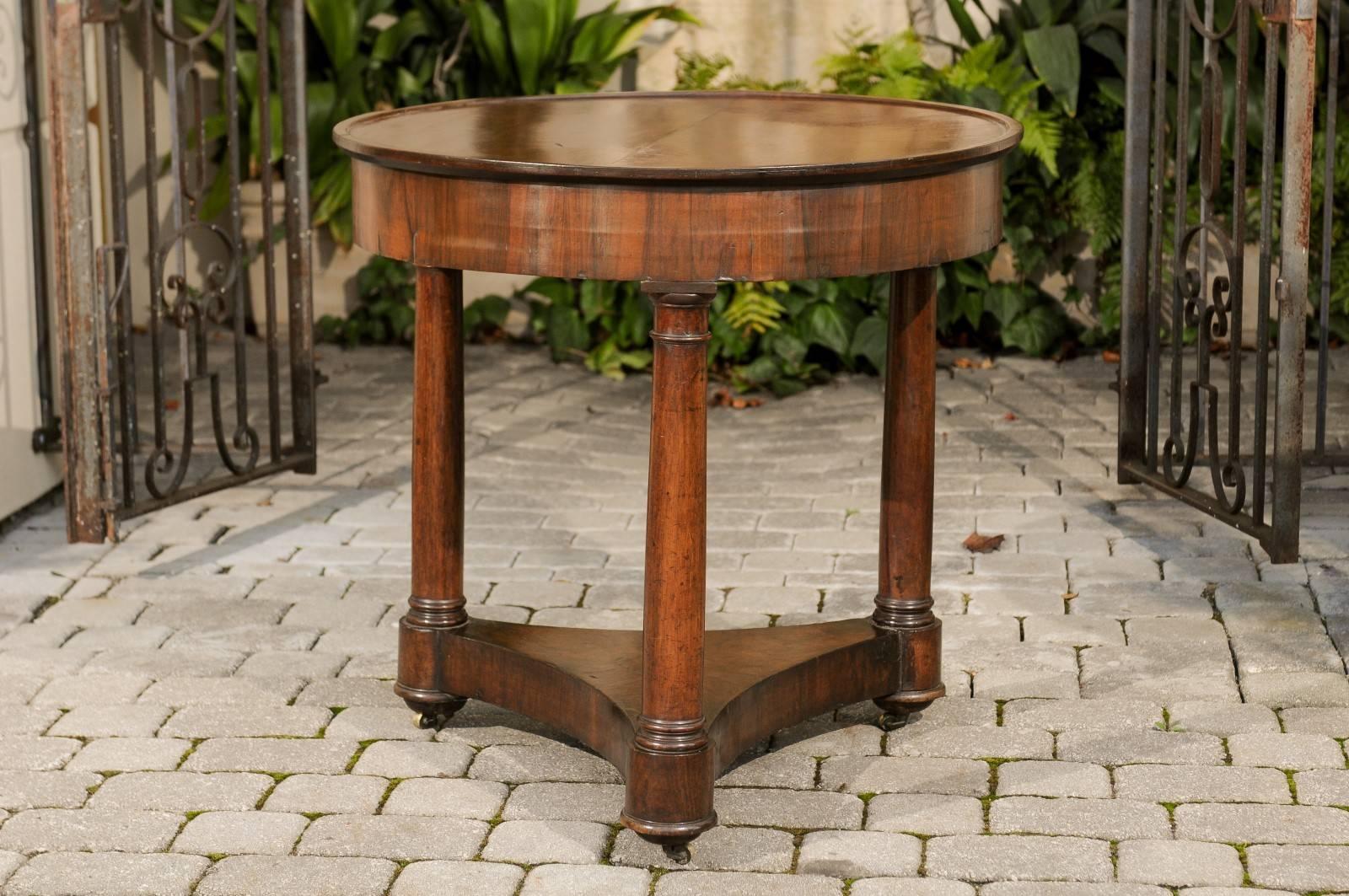 A French Empire style walnut round center table with tripod base raised on casters from the second half of the 19th century. This French centre table features a bookmarked walnut-veneered circular top sitting above a simple apron. The ensemble is