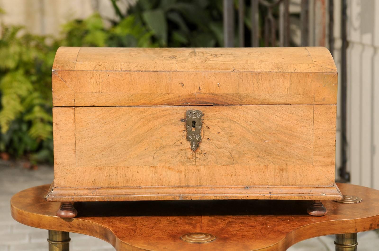 An Austrian Biedermeier decorative box made of burled walnut from the early 19th century with feet. This charming box features a burled walnut body adorned with a crossbanded inlay, creating a subtle visual contrast. The arched lid opens to reveal a