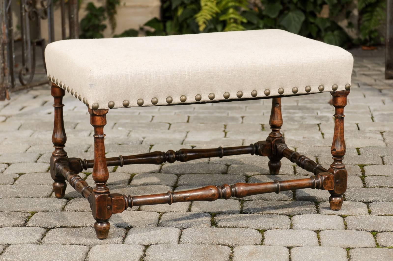 An Italian wooden upholstered bench with turned baluster legs and spindle-shaped side stretchers from the 18th century. This Italian bench features a rectangular linen-upholstered seat with brass nailhead trim, raised on four exquisite baluster
