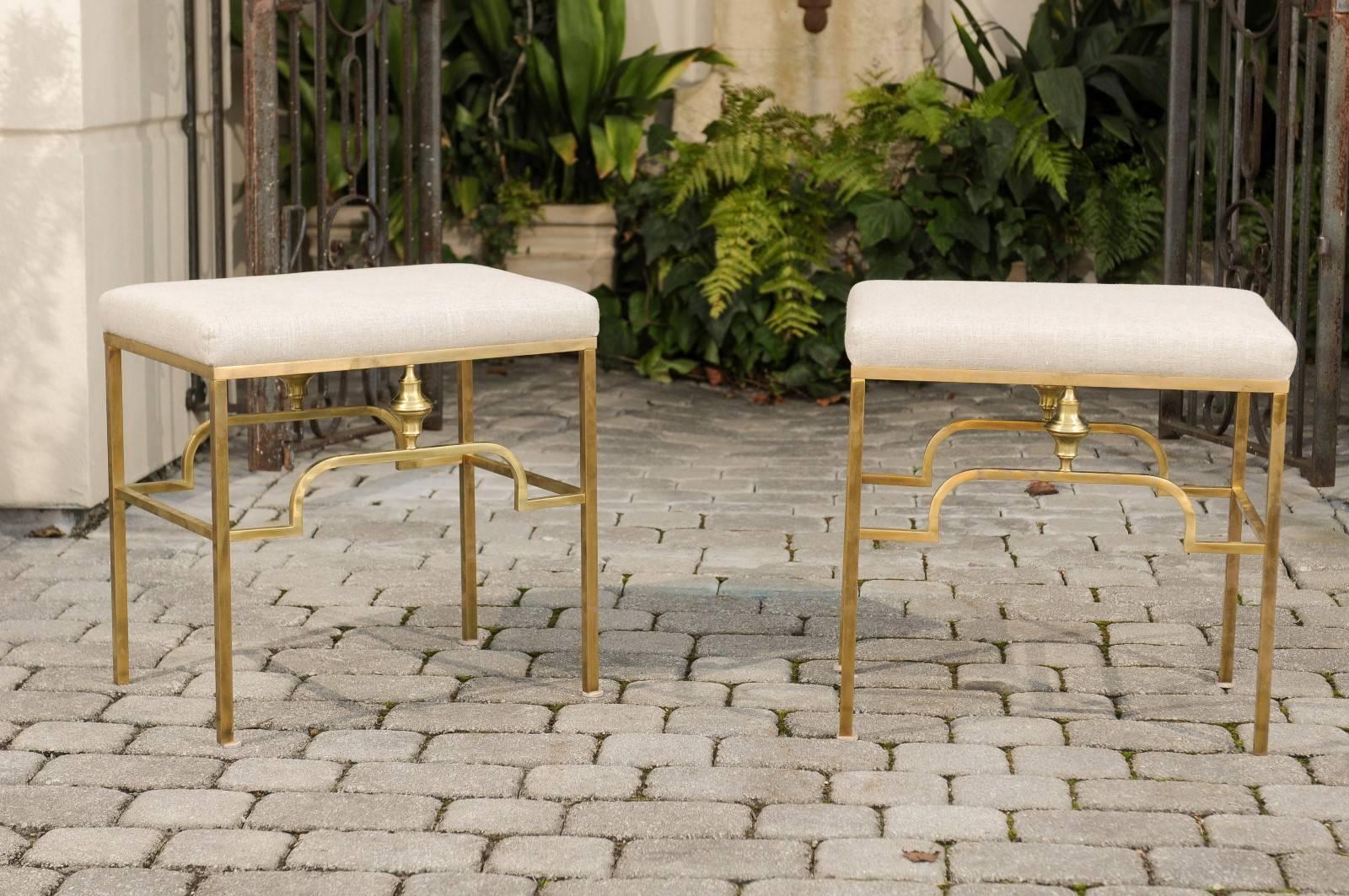 A pair of Italian Mid-Century Modern brass stools with new linen upholstery. Each of this pair of vintage Italian stools features a rectangular linen-covered seat, resting on an Art Deco style brass armature. The clean lines of the base are