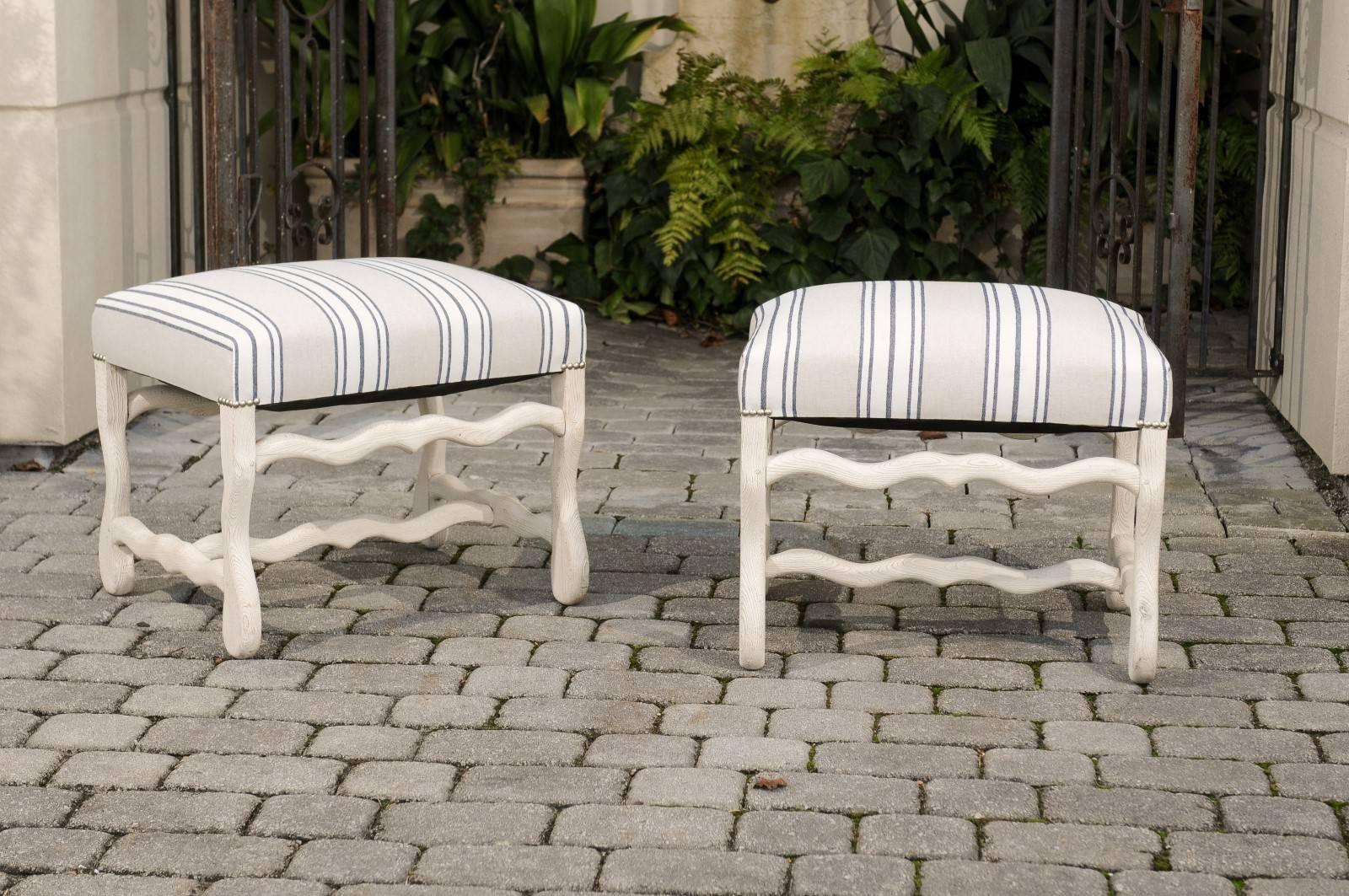 A pair of French bleached wood 'os de mouton' stools with upholstered seats from the early 20th century. Each of this pair of carved wooden stools features a bleached frame, highlighting the grain of the wood beautifully. The rectangular seat is