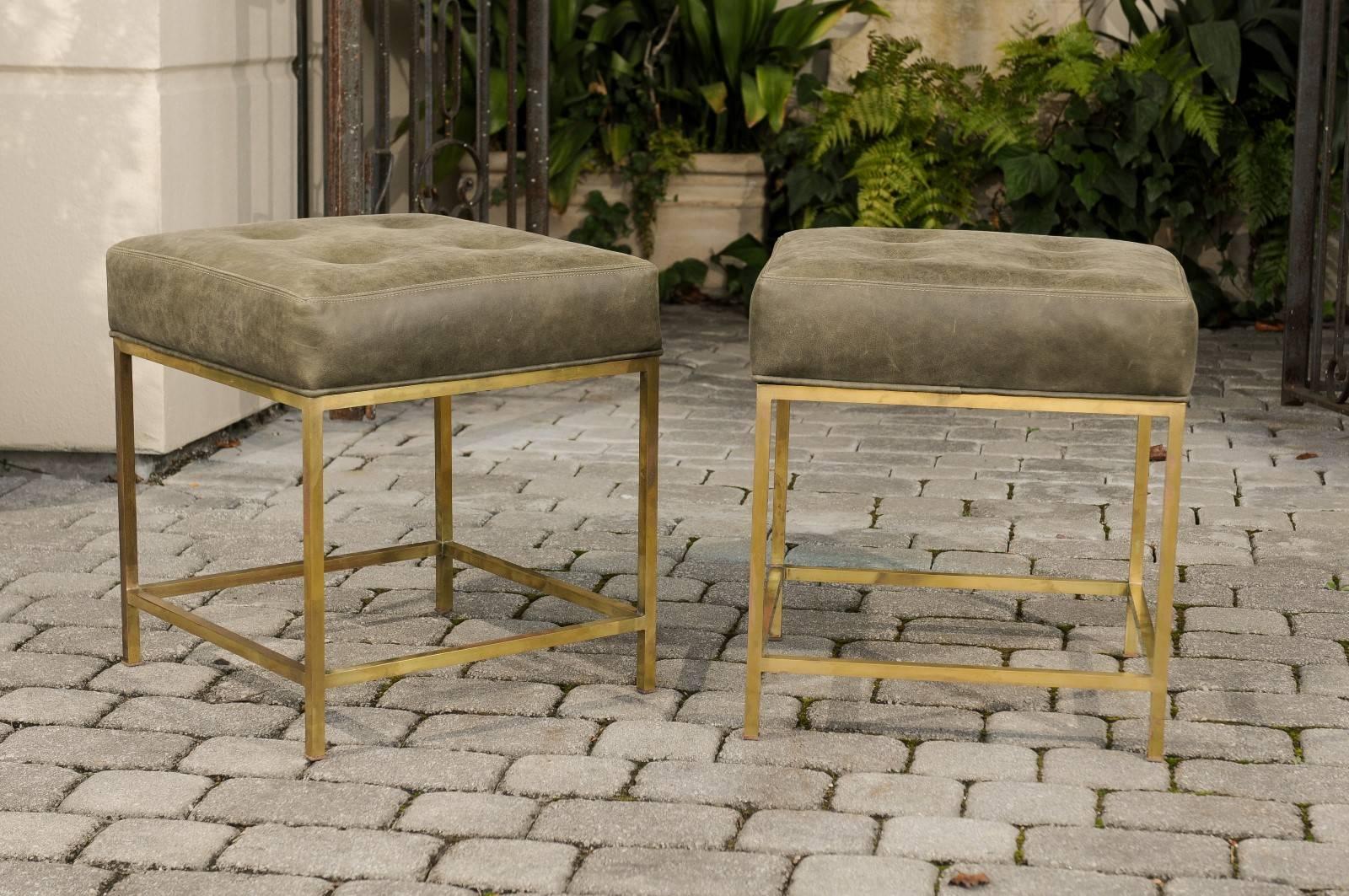 A pair of Italian Mid-Century Modern brass stools from the 1960s with tufted leather upholstery. Each of this pair of Italian stools features a subtle green tufted leather cushion sitting above a brass armature. Showcasing a linear Silhouette, each