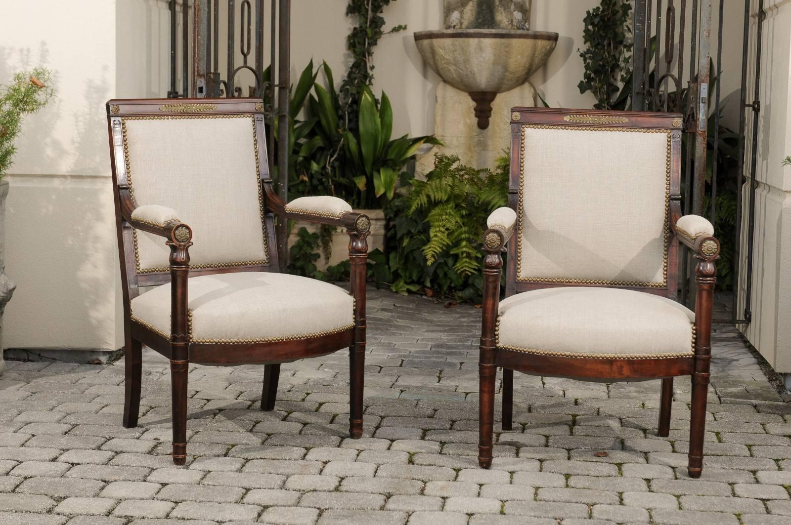 A pair of English Empire Revival upholstered armchairs from the 19th century. Each of this pair of English Empire armchairs features a slightly slanted square back with straight open arms resting vertically on two straight cylindrical legs in the