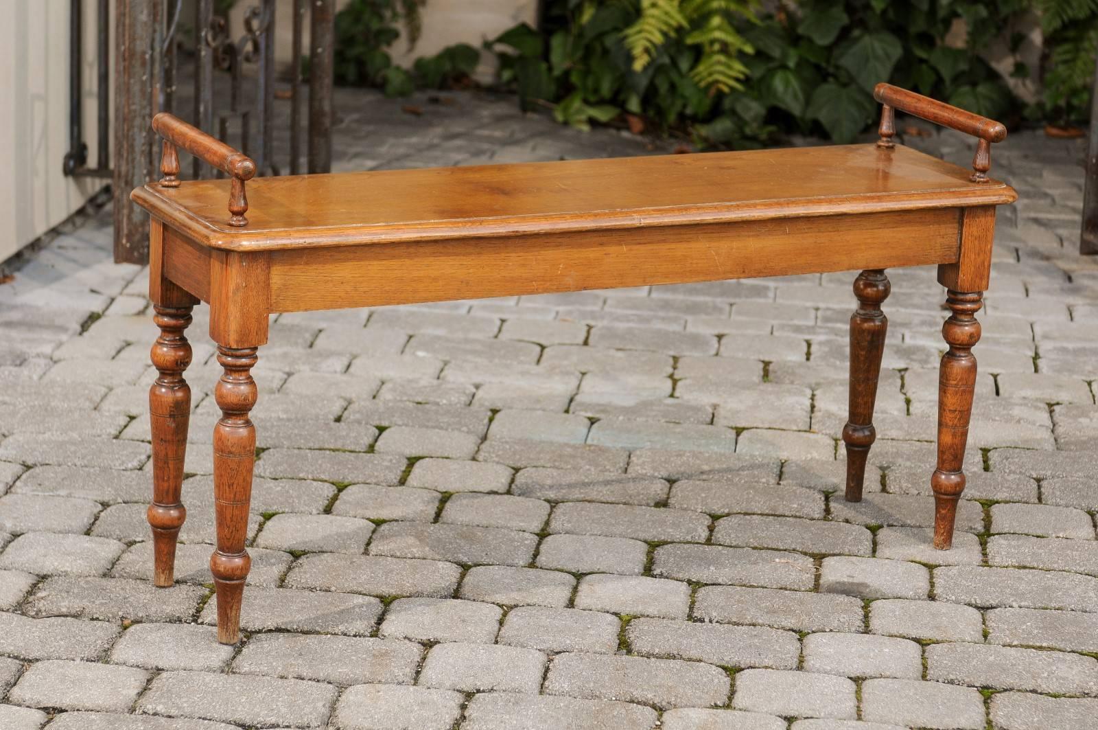 An English oak backless hall bench with cylindrical armrests, rectangular wooden seat and turned legs from the early 20th century. This English hall bench features a single-plank rectangular seat with rounded edges, flanked with two cylindrical arm