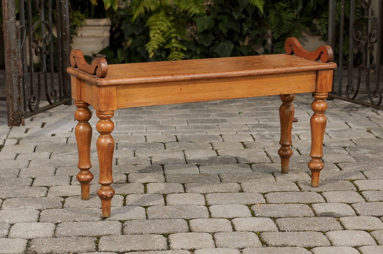 An English oak hall bench with turned legs and curled arm supports from the turn of the century. This English oak hall bench features a rectangular single plank wooden seat with beautiful grain, adorned with two exquisite curled arm supports. The