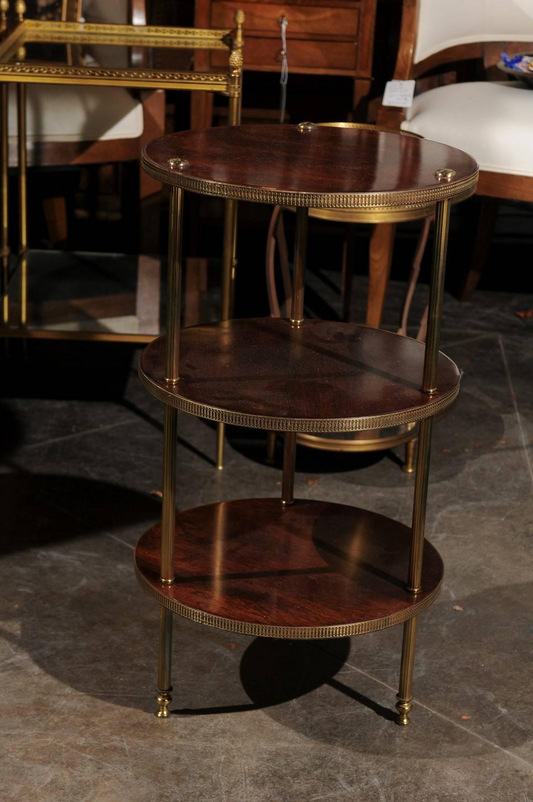 A vintage Italian three-tiered wood and brass stand from the midcentury. This Italian stand features three circular wooden shelves with fluted brass molding. Each shelf is secured to three brass supports, running from the top to the bottom of the