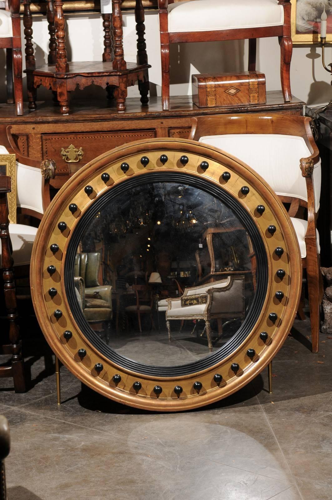 An English vintage gilt and ebonized bullseye mirror from the 1950s. This English mirror from the mid-20th century features a circular flat mirror plate surrounded by an ebonized wood molding. The outer frame is made of giltwood and adorned with