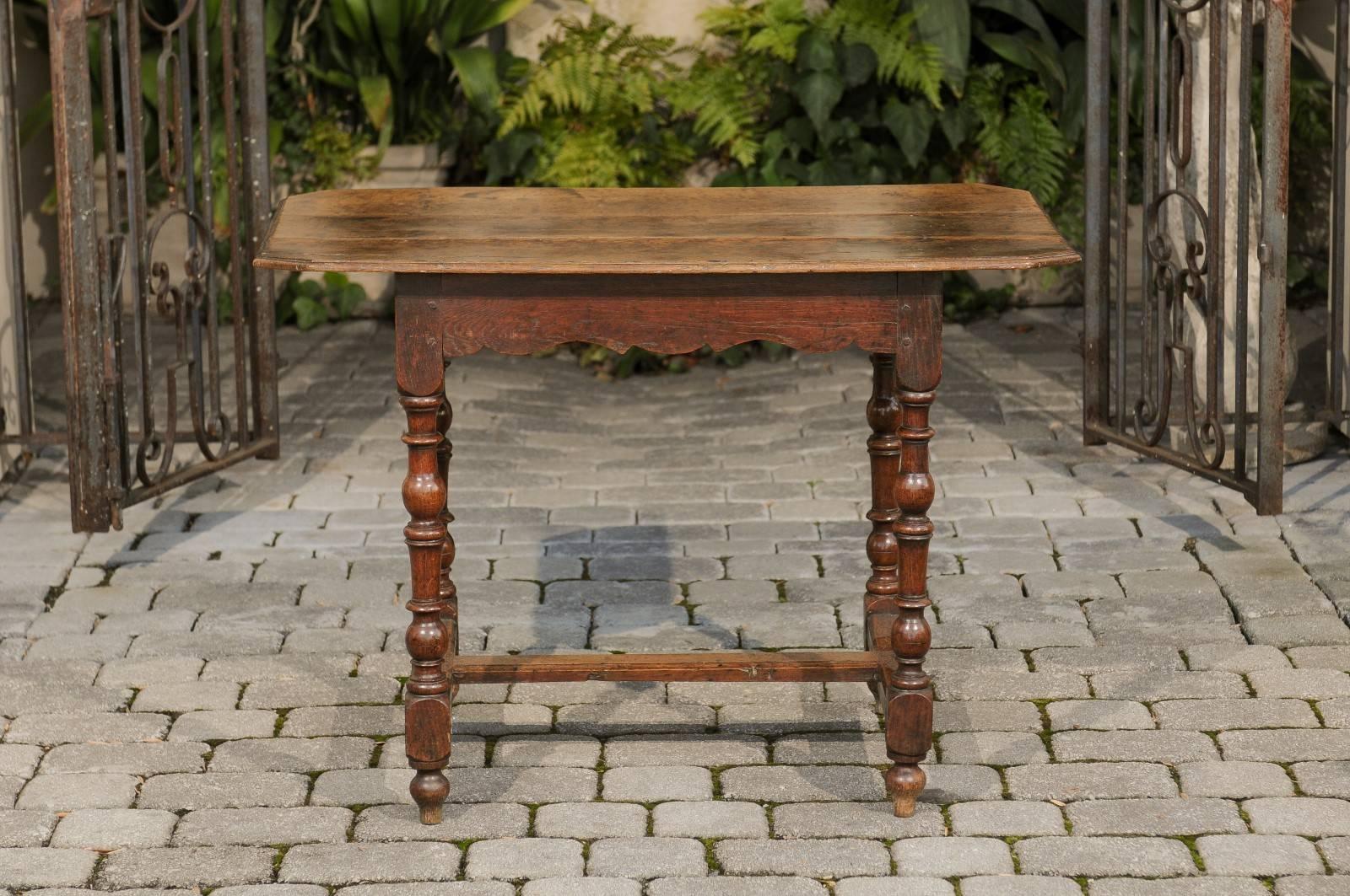 A French oak side table with turned legs and cross stretcher from the late 18th century. This French side table features a rectangular top with canted corners sitting above a nicely carved apron. The table is raised on four turned legs resting on
