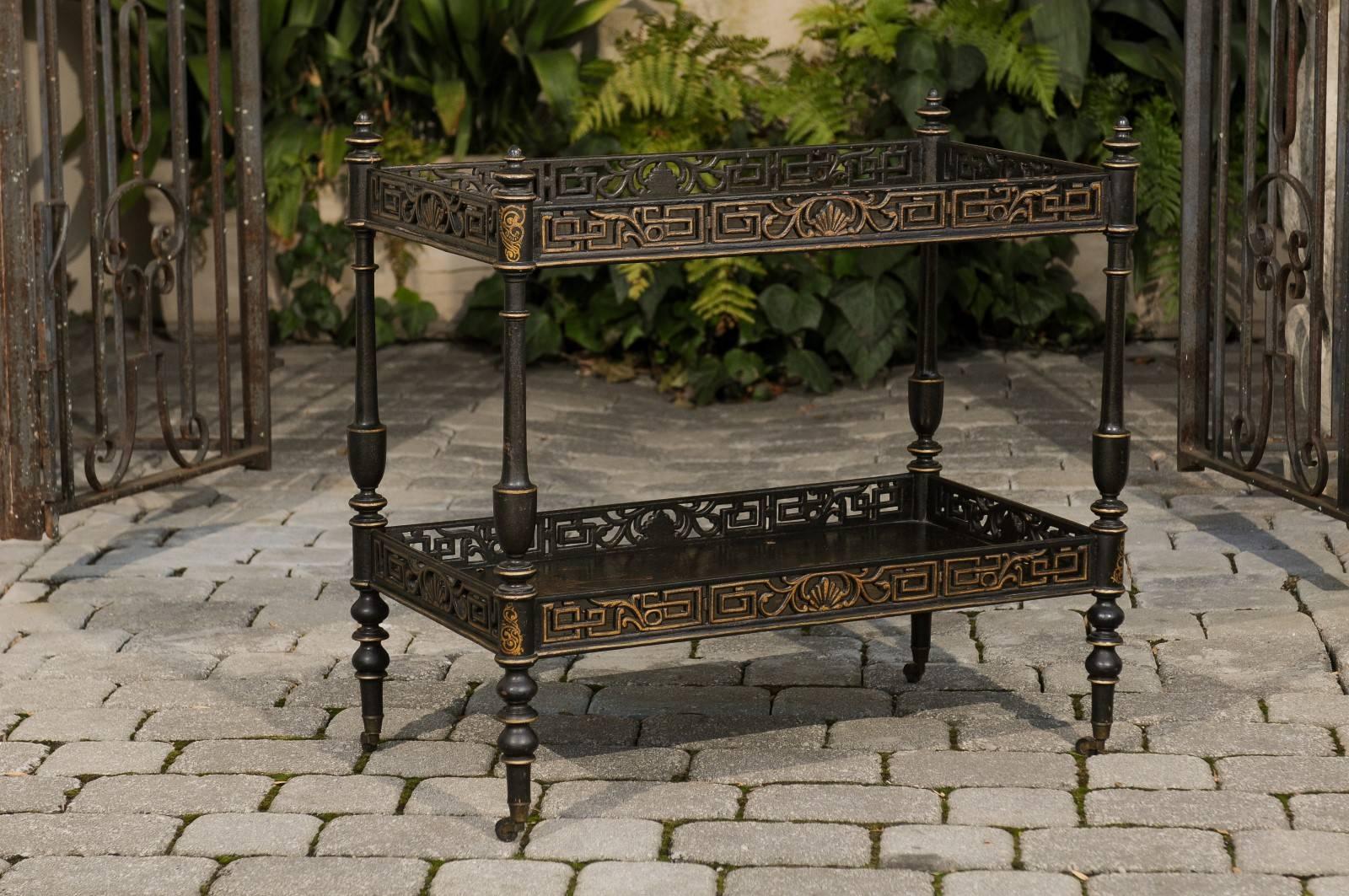 An English chinoiserie revival trolley with two shelves from the early 20th century. This English trolley features an exquisite ebonized wood body, delicately highlighted by giltwood accents. The upper tray is adorned with delicate chinoiserie