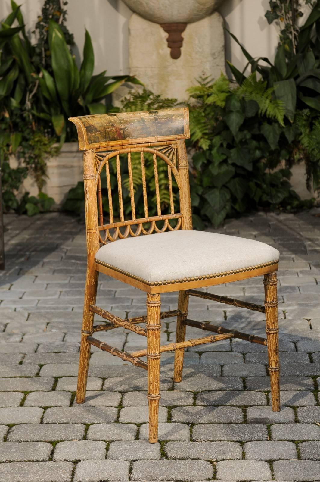 An English period Regency single wooden side chair with painted scene and upholstered seat over cane from the early 19th century. This English side chair features a faux-bamboo frame, adorned with a curved top rail painted with a scene showing a