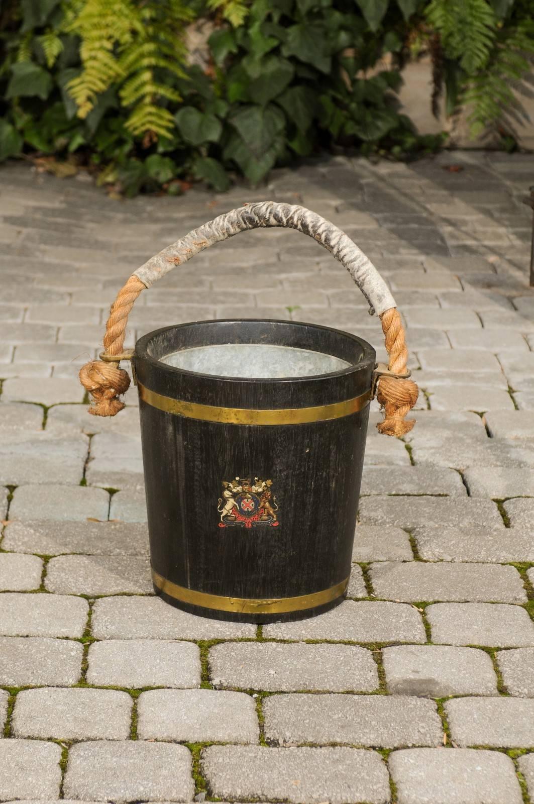 An English Champaign bucket made of oak with copper bands and a coat of arms from the late 19th century. This oak bucket retains its tin liner which is intended to protect the wood. The bucket is made of dark oak slats secured by two copper bands. A