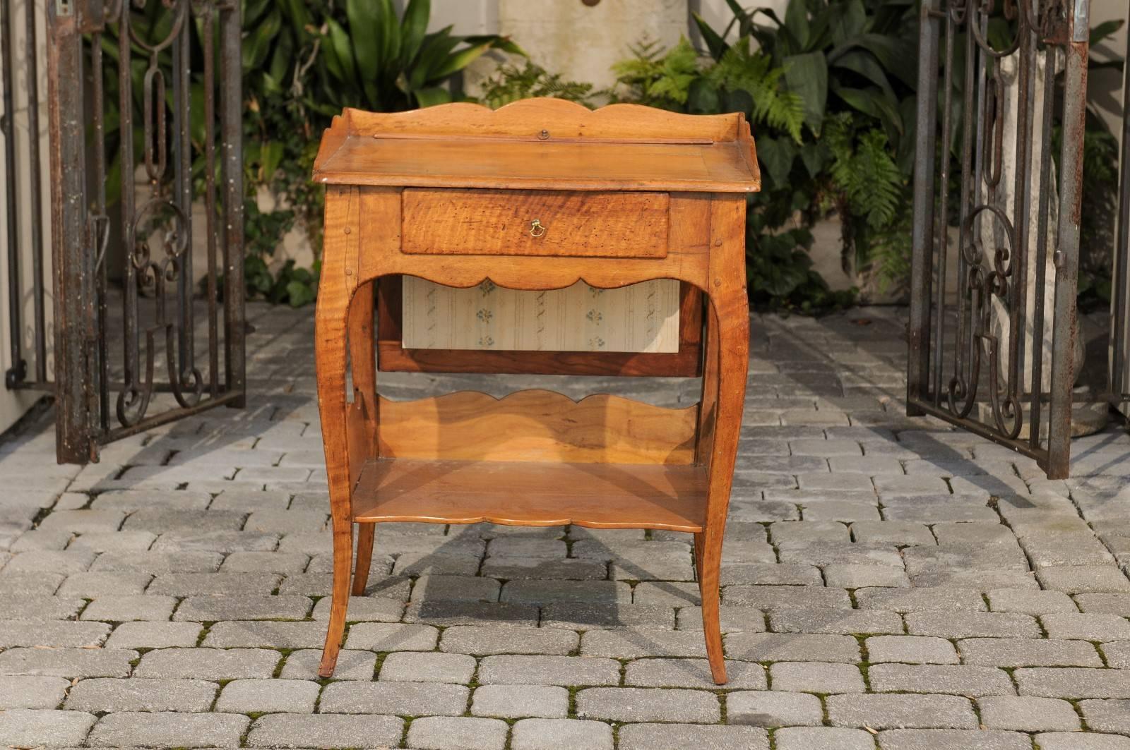 A French fruitwood side table with firescreen, single drawer and lower shelf from the early years of the 19th century. This French fruitwood side table features a rectangular top adorned with a nicely scalloped three-quarter wooden gallery, sitting