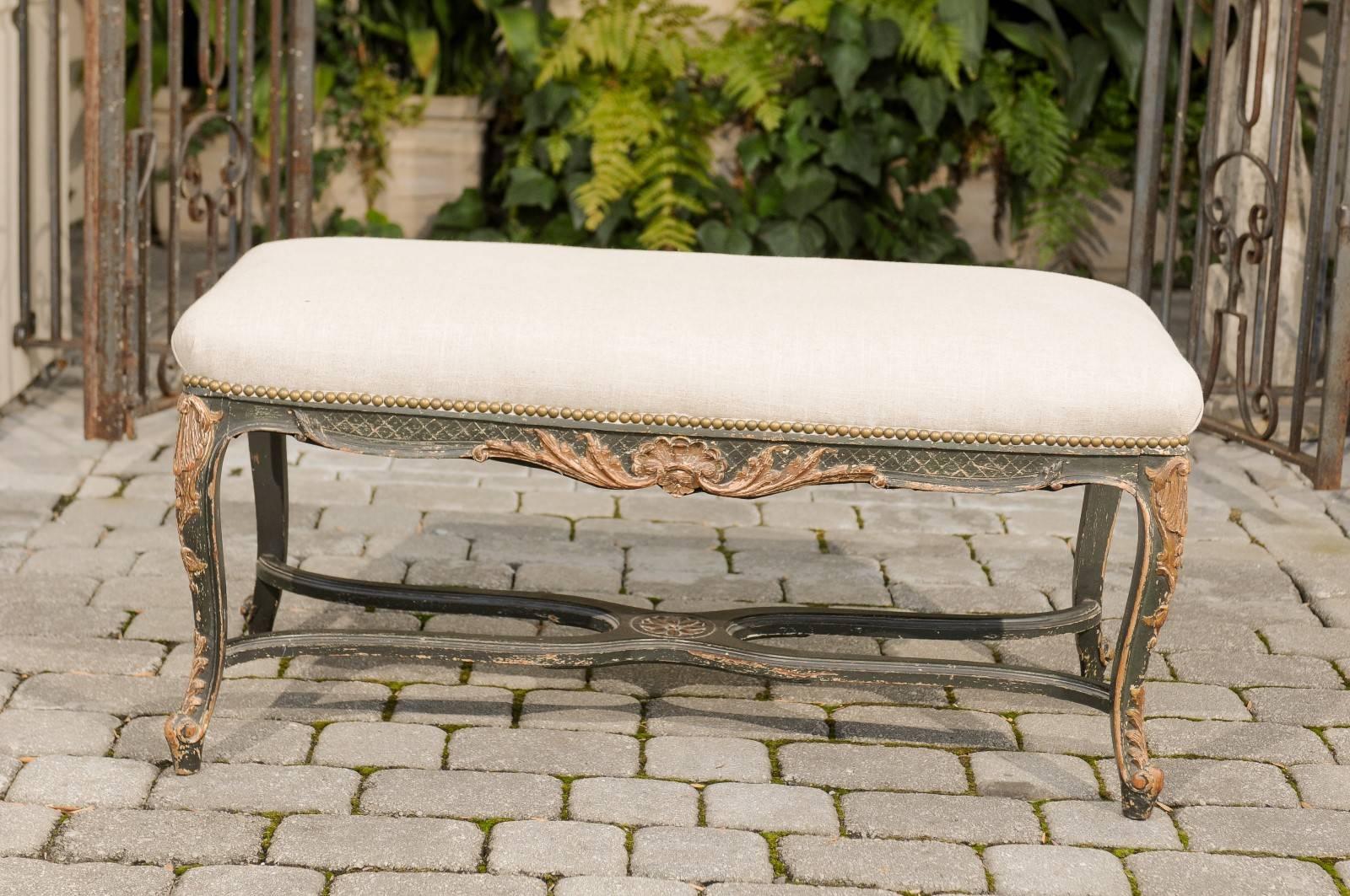 A French painted and carved wooden Louis XV style bench from the late 19th-early 20th century. This exquisite French Louis XV style bench features a rectangular backless seat, covered with a simple linen upholstery secured by a brass nailhead trim.