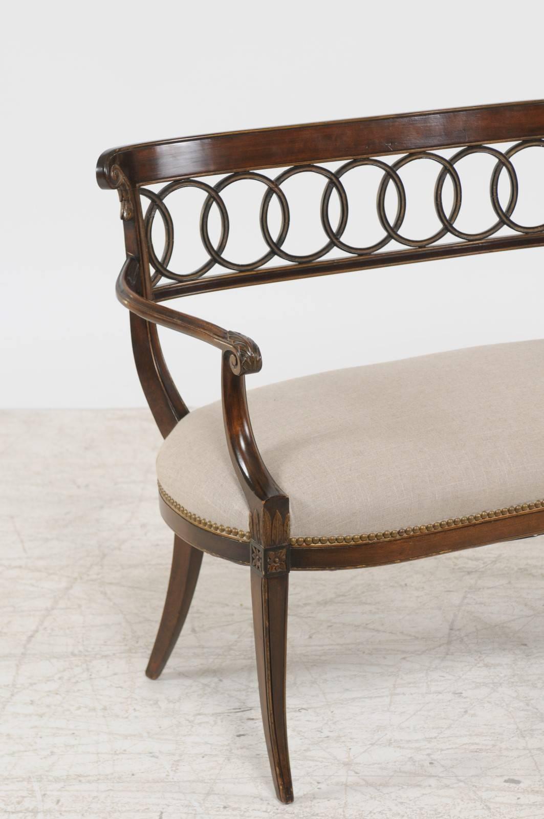 A pair of Italian carved walnut parcel gilt benches with intertwined ring pierced backs, scrolled arms, saber legs and new upholstery. Each of this pair of Italian benches features an exquisite back, delicately curved and carved with eye catching
