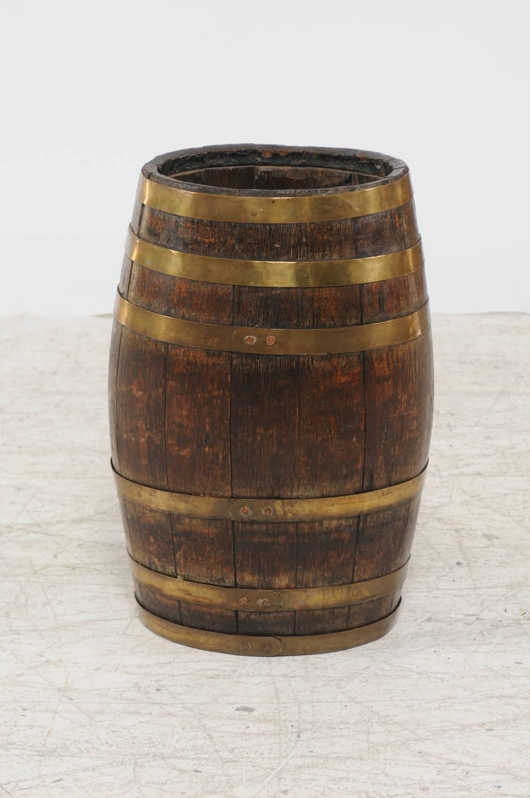 A tall English oak barrel with brass straps from the late 19th century. This English barrel features a sturdy oak body made of various slats, whose vertical lines are contrasted by the horizontal brass straps that accentuate the piece. The
