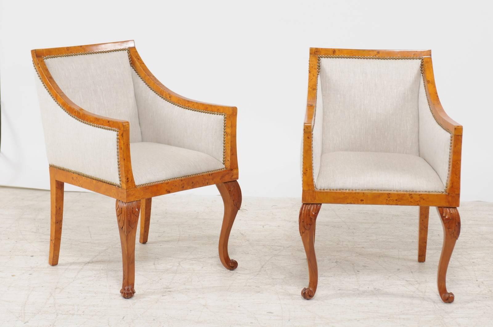 A pair of mid-19th century Biedermeier Austrian burled wood bergère chairs with new linen upholstery and brass nailhead trim. Each of this pair of Austrian armchairs features the typical traits of the Biedermeier period. The burled blond wood and