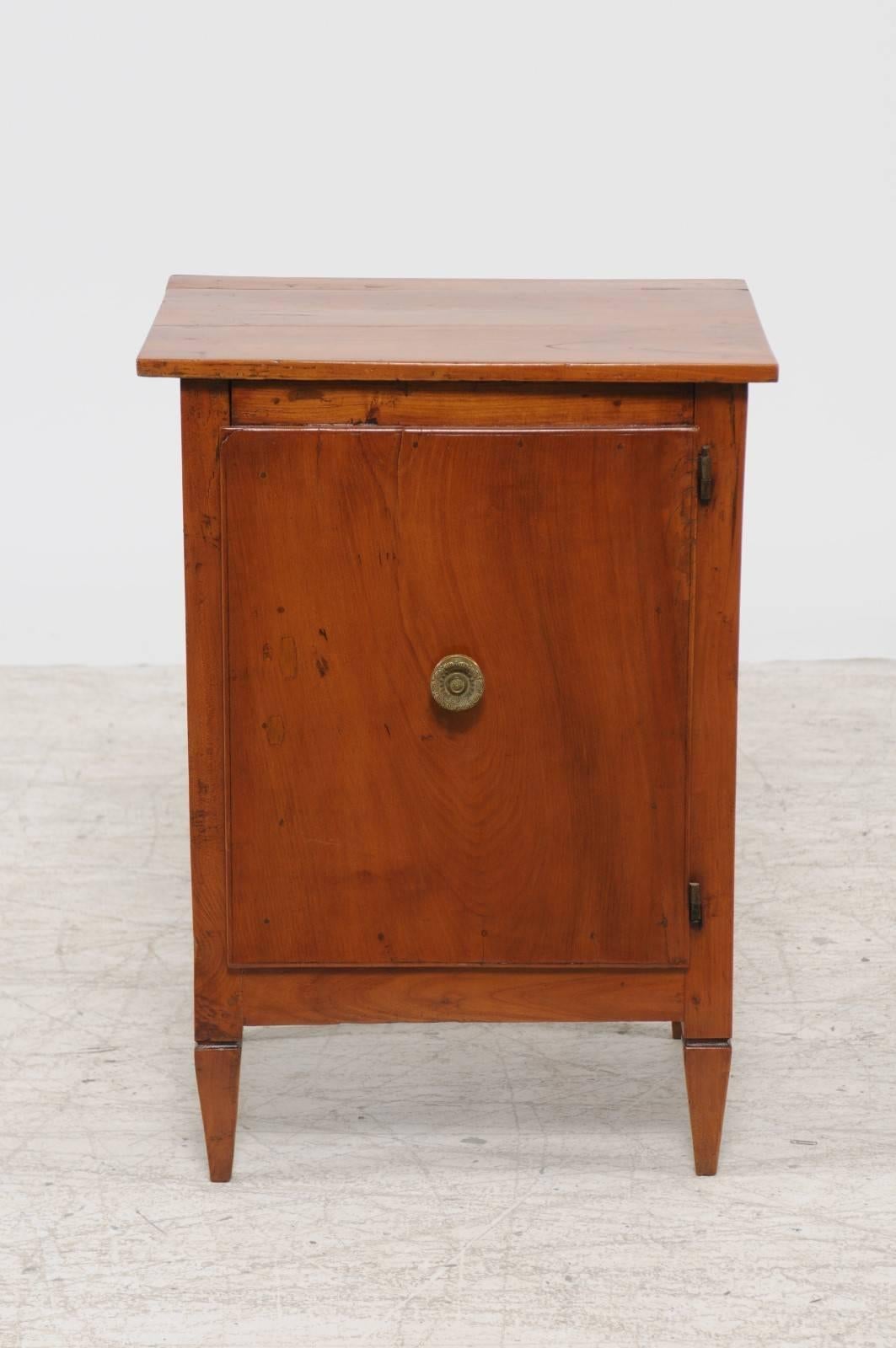 An Italian neoclassical period walnut single-door petite cabinet from the early 19th century. This Italian small size cabinet features a rectangular planked top sitting above a single door opening with a round bronze pull. This door opens to reveal