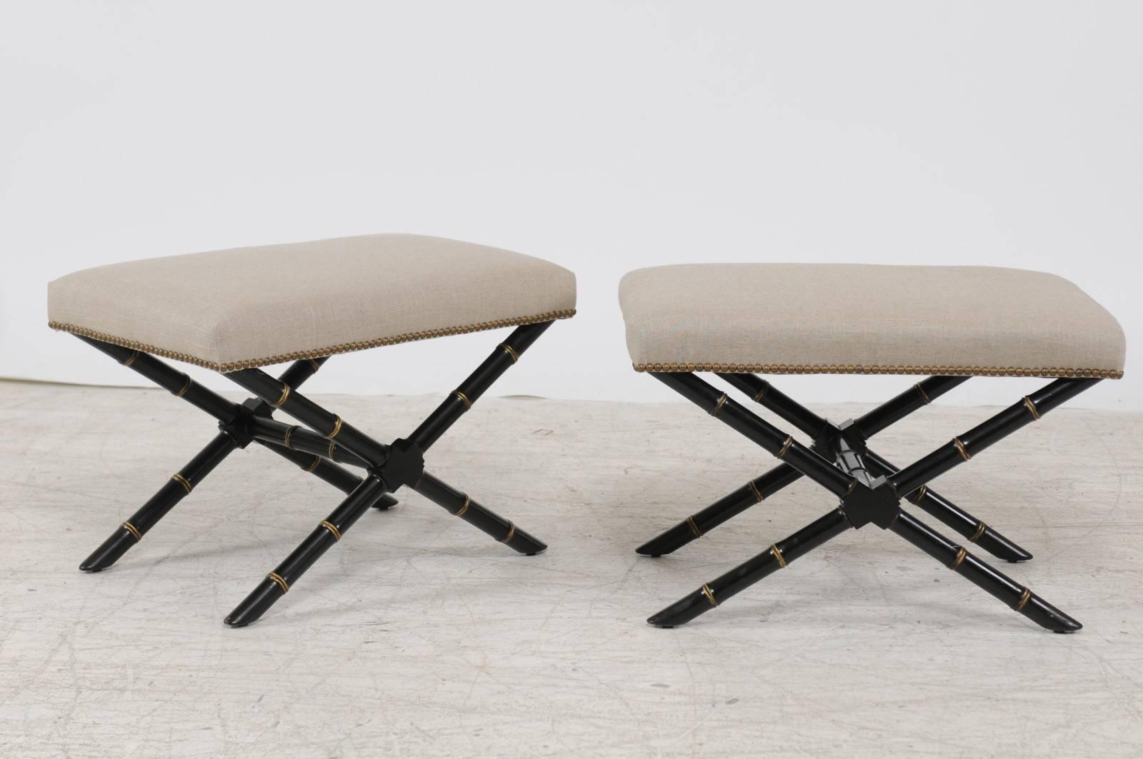 A pair of French ebonized wood faux-bamboo X-frame stools from the mid-20th century with newly upholstered seats. Each of this pair of French stools features a rectangular seat, reupholstered with a simple linen fabric, accented on the trim with