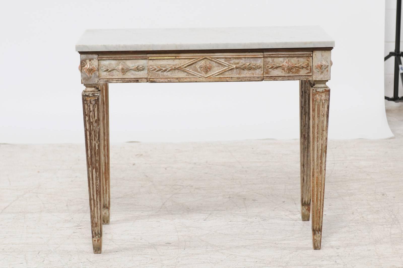 A Swedish Neoclassical style white marble top with single drawer, distressed paint and tapered legs from the second half of the 19th century. This Swedish console table features a white rectangular top sitting above an exquisitely carved base. The
