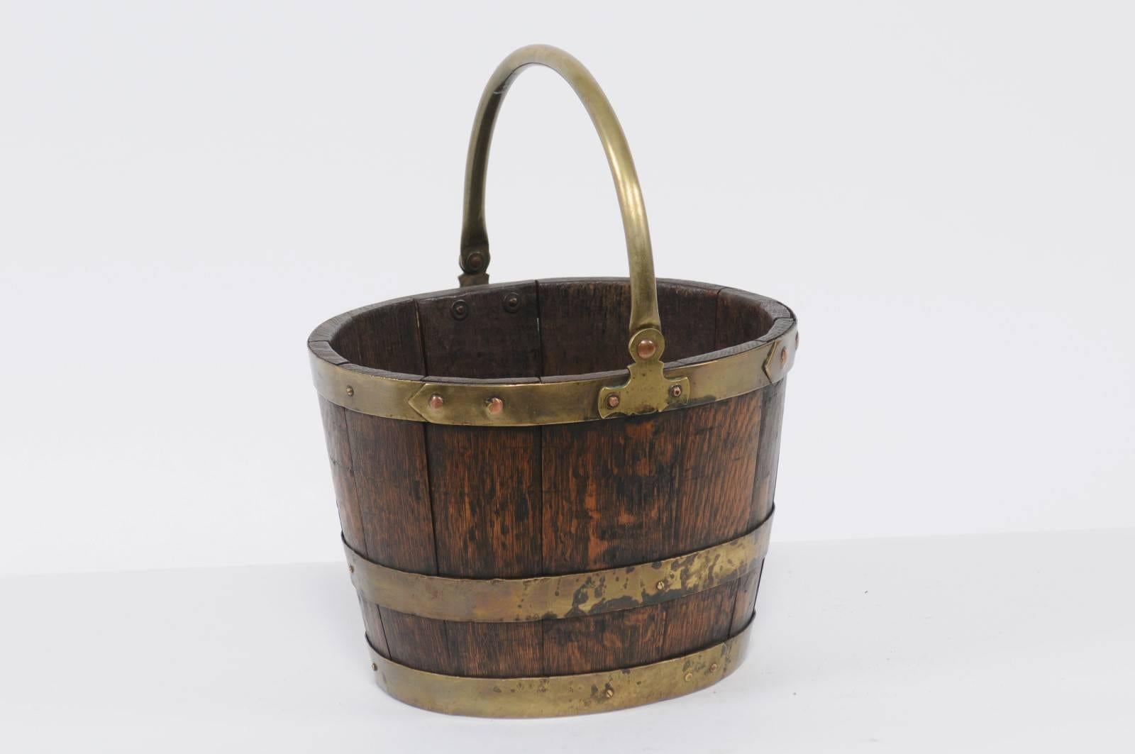 An English oak and brass bucket with loop handle from the late 19th century. This English bucket features a body made of vertical oak slats, strengthened by a series of horizontal brass rings. With its simple clean lines and two colors contrasting
