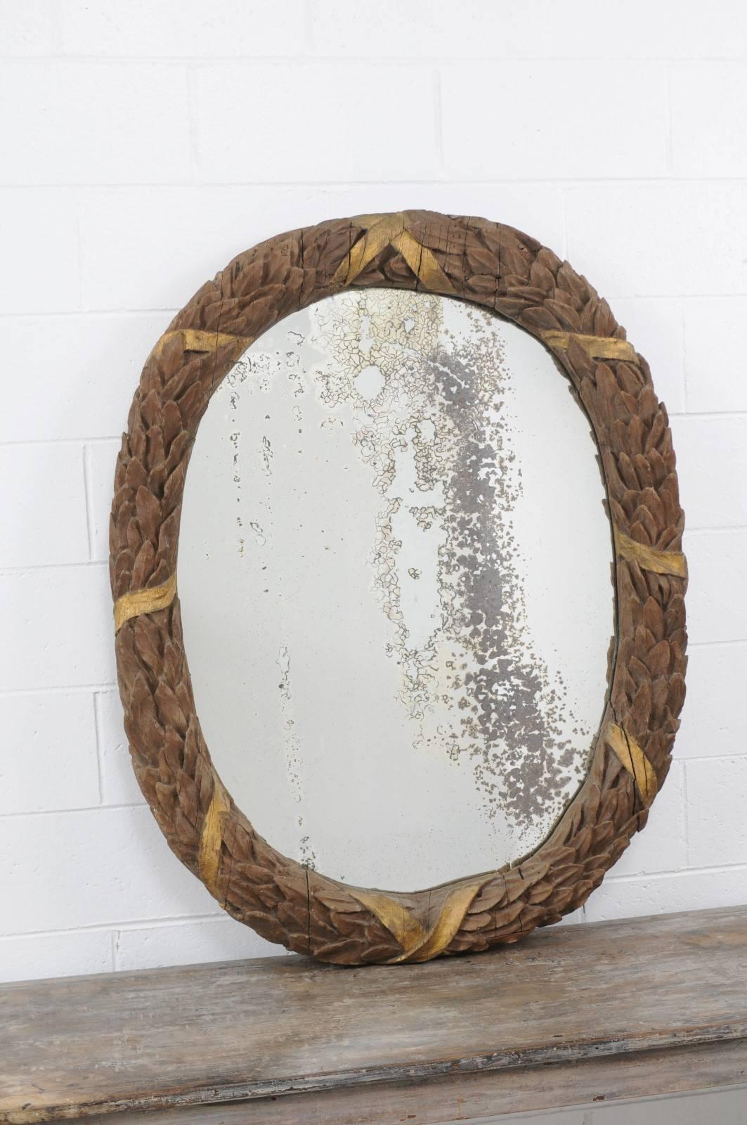 A neoclassical style French oval carved oak mirror with ribbon-tied wreath motif from the late 19th century. This French carved oak mirror features an exquisite oval frame, adorned with a parcel-gilt ribbon-tied wreath, surrounding a nicely aged