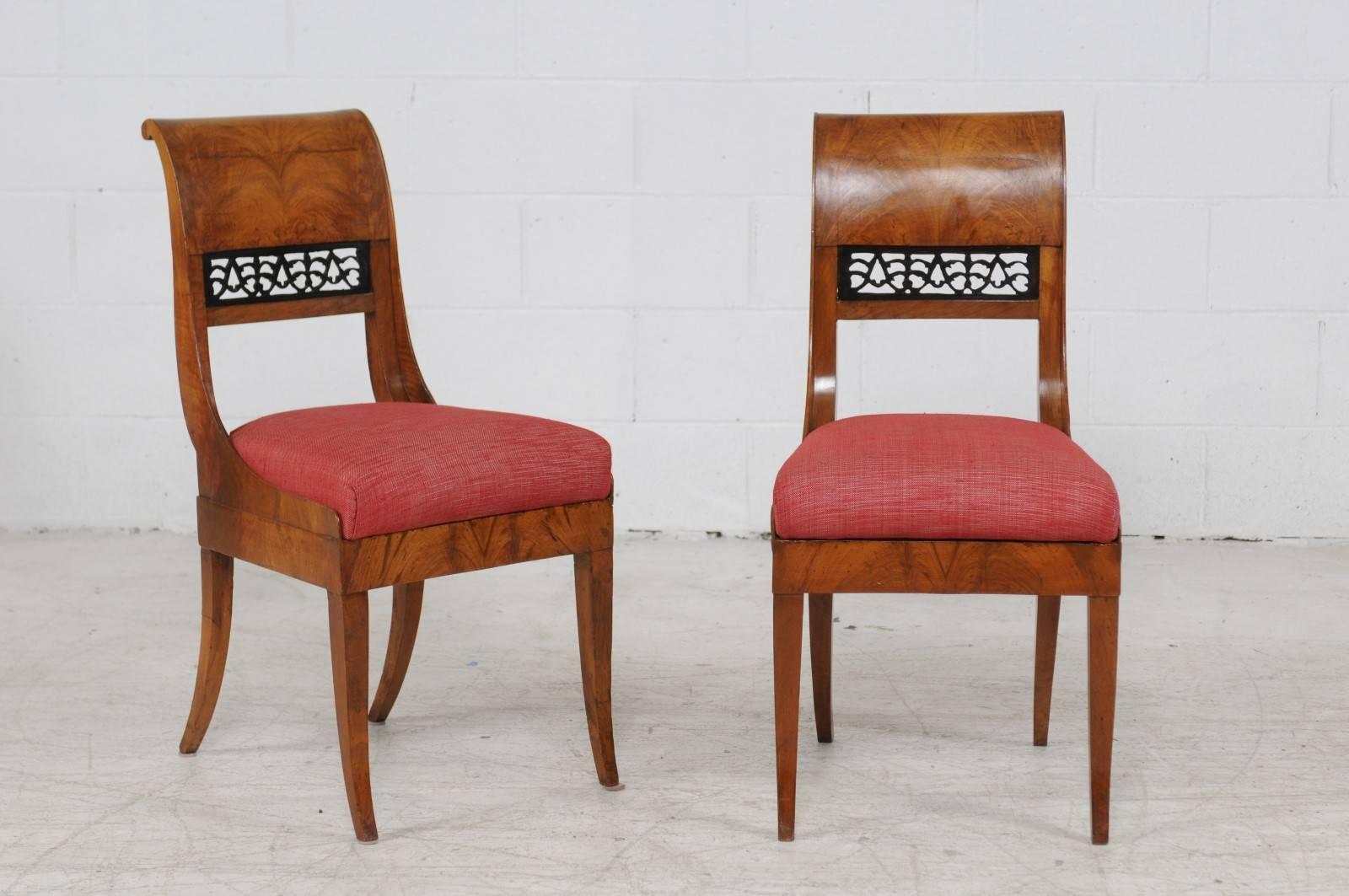 A set of four Austrian Biedermeier period side chairs from the first half of the 19th century with red upholstery. Each of this set of Biedermeier chairs features an exquisite bookmarked veneered body with a delicately out-scrolled back, adorned