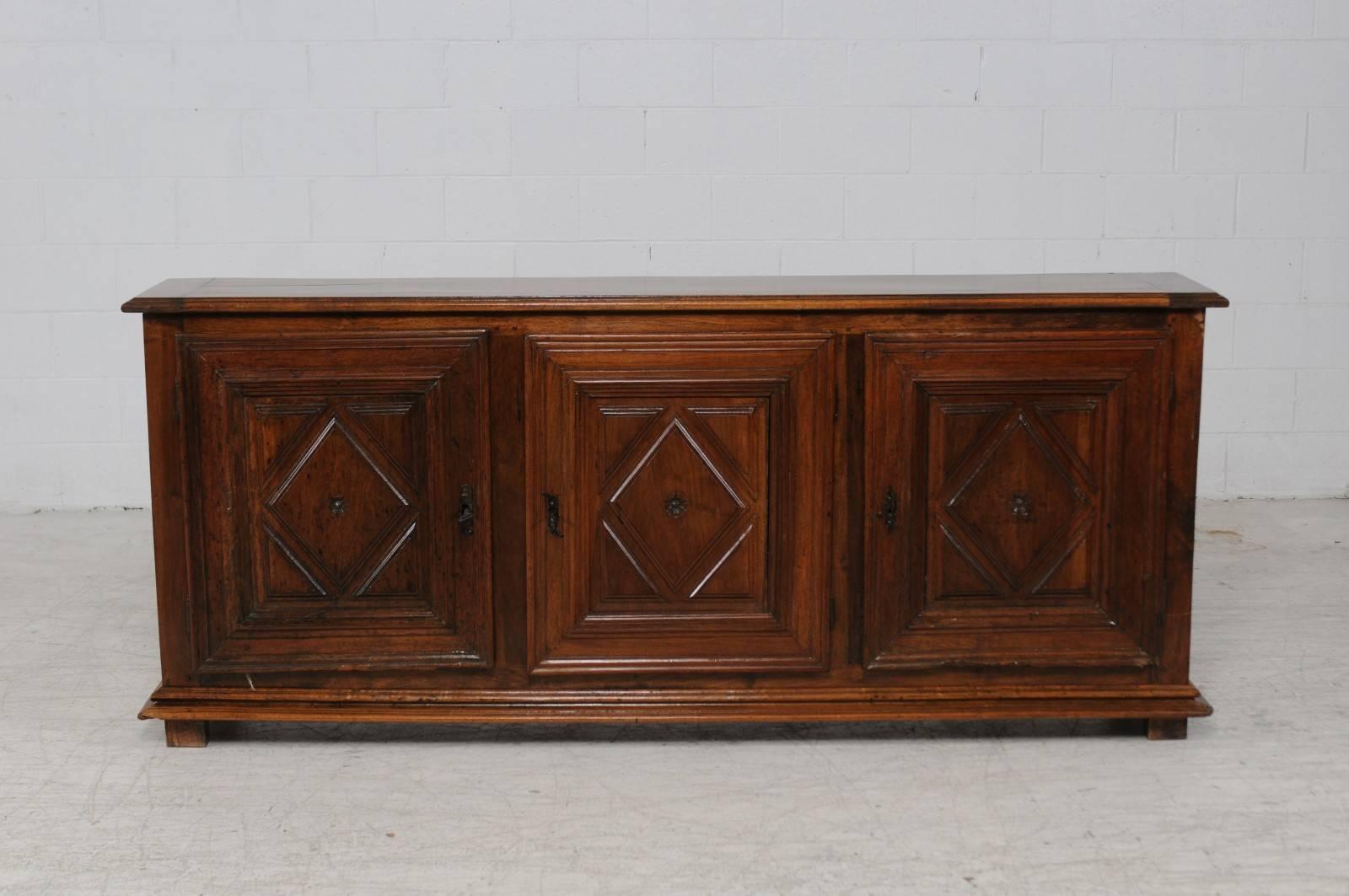 An Italian three-door chestnut enfilade from the early 19th century. This Italian long buffet features a rectangular top with molded edges sitting above three beautifully carved doors. Each door is made of molded frames surrounding a vertical