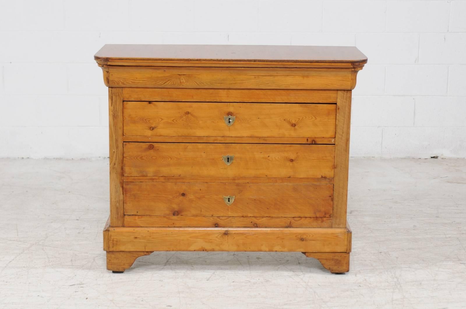 A French Louis-Philippe style pine four-drawer commode from the late 19th century. This French commode features a rectangular top with rounded corners in the front sitting above a frieze pull-out drawer concealed in the upper rail. Three larger