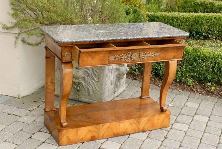 A mid-19th century French burl walnut Louis-Philippe console table with a rectangular variegated grey marble top over a doucine bronze-mounted frieze drawer. Two bronze carved rosettes flank the pull-out drawer divided in three-compartments and