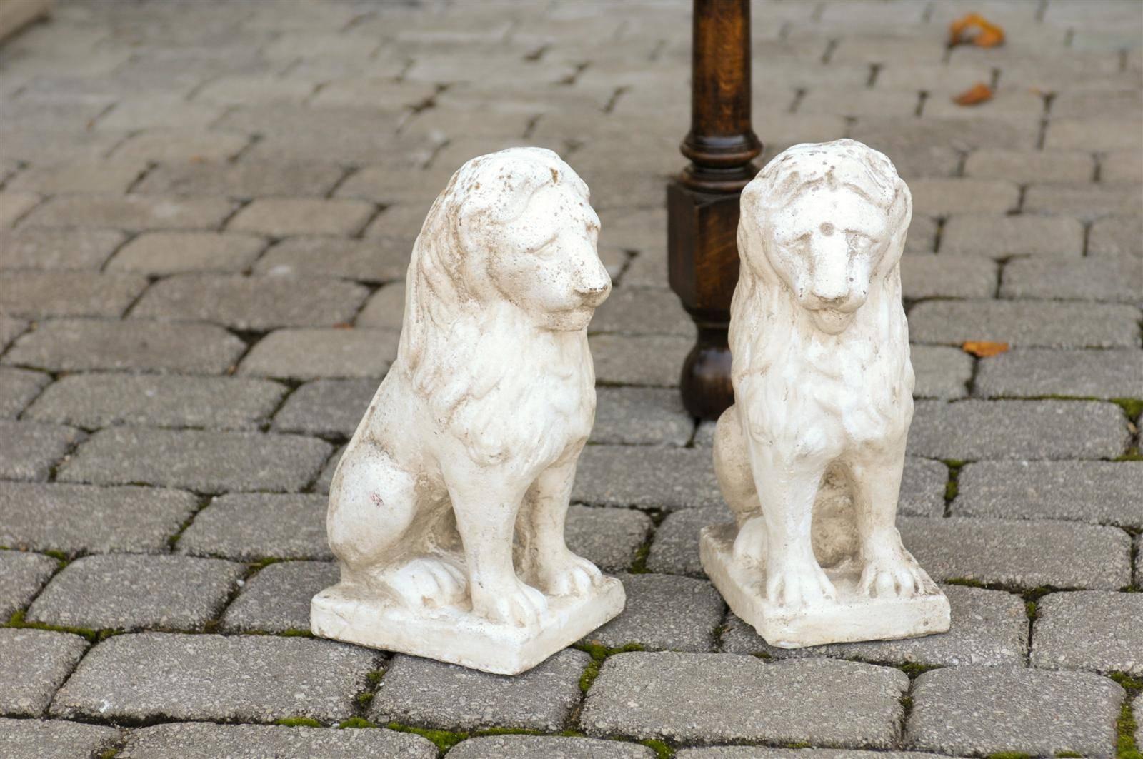 This pair of petite French lion sculptures from the mid 20th century features two lions made of composition, peacefully sitting on a base. Depicted with great simplicity, the lions are guardians, with their tail neatly tucked in their back. Light in