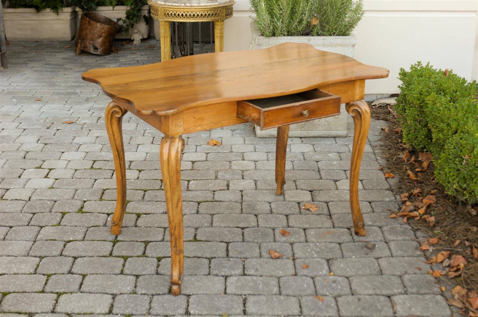 This French Louis XV style mid-19th century wooden desk / writing table features a beautifully curvy three-plank top over a simple apron with a single drawer. The table is raised on four elegant cabriole legs, raised on hoofed feet. With its blond