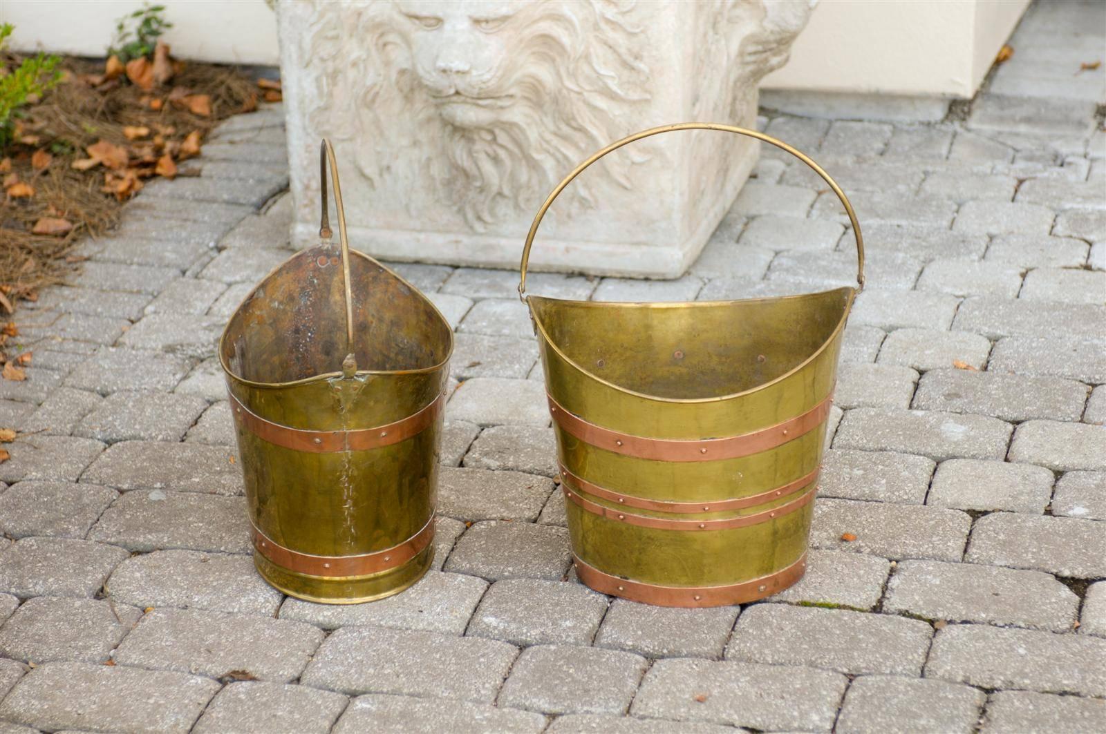 An English oval brass bucket with handle from the early 20th century.  The rim of the brass bucket is curved on two sides with the high point securing the handle. This creates a wide shape allowing for larger items to be placed in the bucket. 