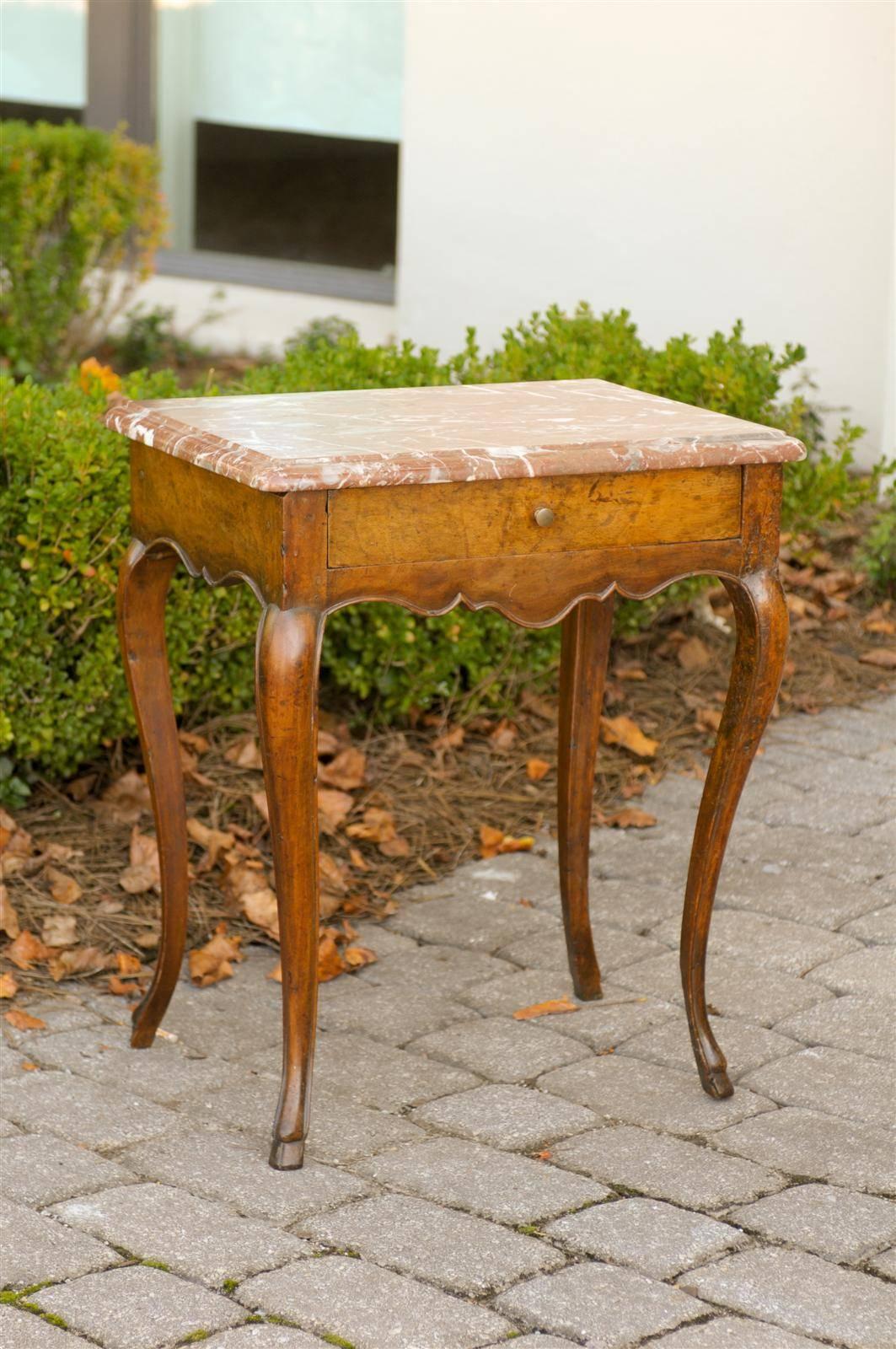 This exquisite French Louis XV style side table from the late 18th century, features a chamfered rectangular royal red and white veined marble top over a single hand-cut, dovetailed drawer. The table is raised on four delicate cabriole legs with