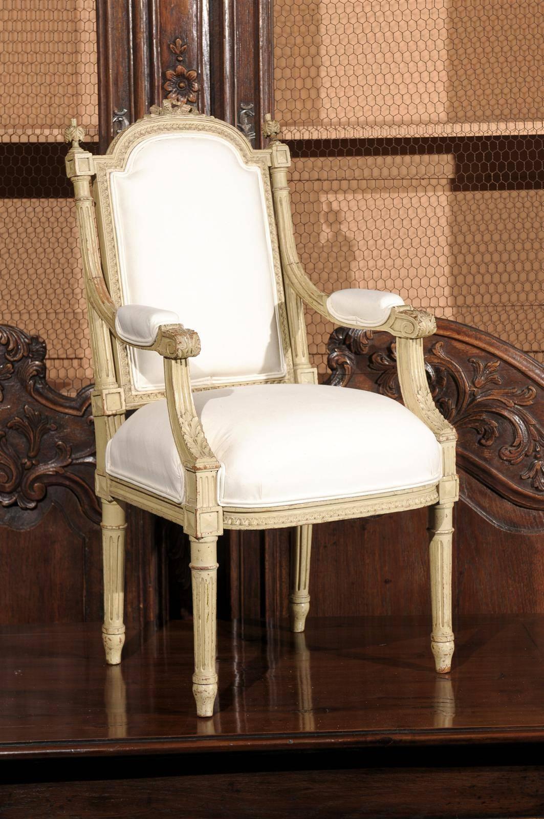 This French painted child’s chair from the early 20th century features a lovely carved and slightly slanted back with a Louis XVI style knot in the crest, flanked with two unusual finials resting on block joints at the top of fluted arms. The