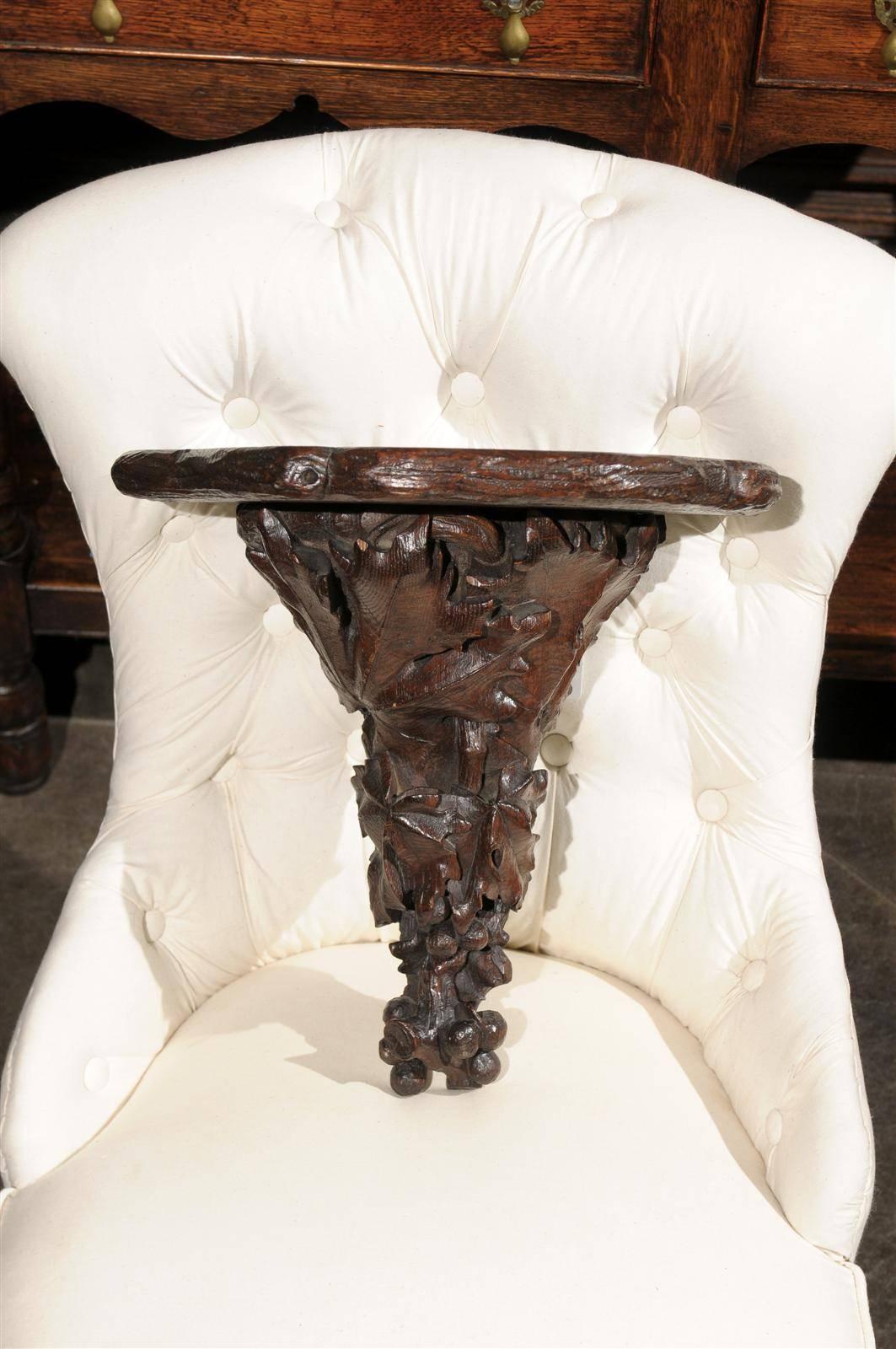 This pair of German carved wood black forest brackets from the turn of the century features a simply shaped carved top over a nicely decorated carved base adorned with oak leaves and grapes. Perfect for receiving small decorative objects such as a