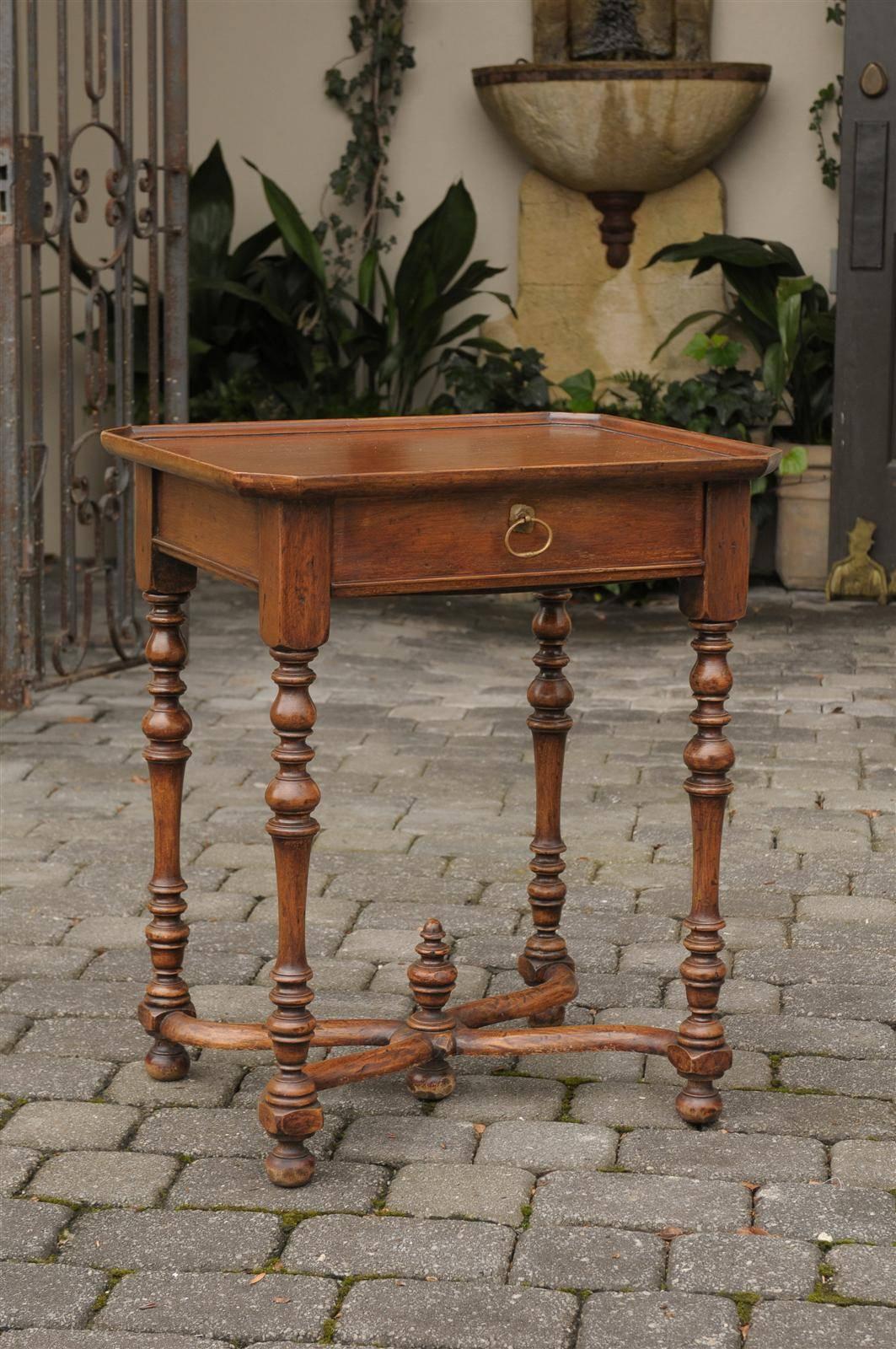 This French side table from the turn of the century features a rectangular tray top with canted corners over a single drawer with brass pull. The table is raised on four turned legs, connected to one another with a lovely x-shaped cross stretcher,