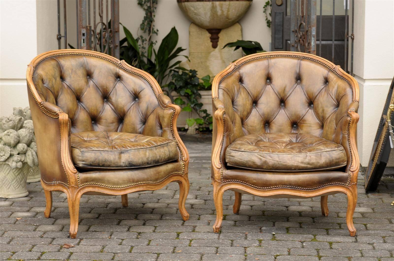 This pair of French Louis XV style bergeres features lovely colored leather upholstery, tufted in the back with nailhead trim. The wraparound backs, as well as the seat cushions, offer great comfort to the sitter. The curviness, typical of the Louis