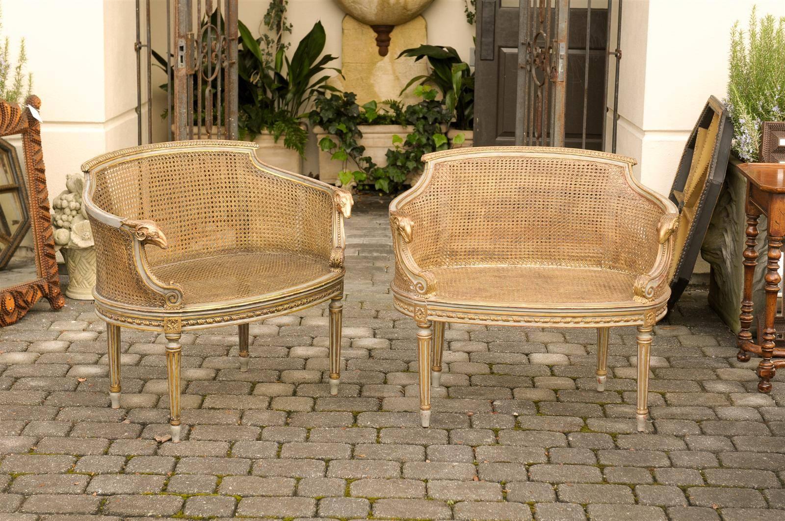 This pair of French Louis XVI style barrel-back chairs features exquisite cane backs and seats. The curved backs provide great support for the sitter to rest comfortably. The arms are beautifully adorned with carved rams heads and Baroque style