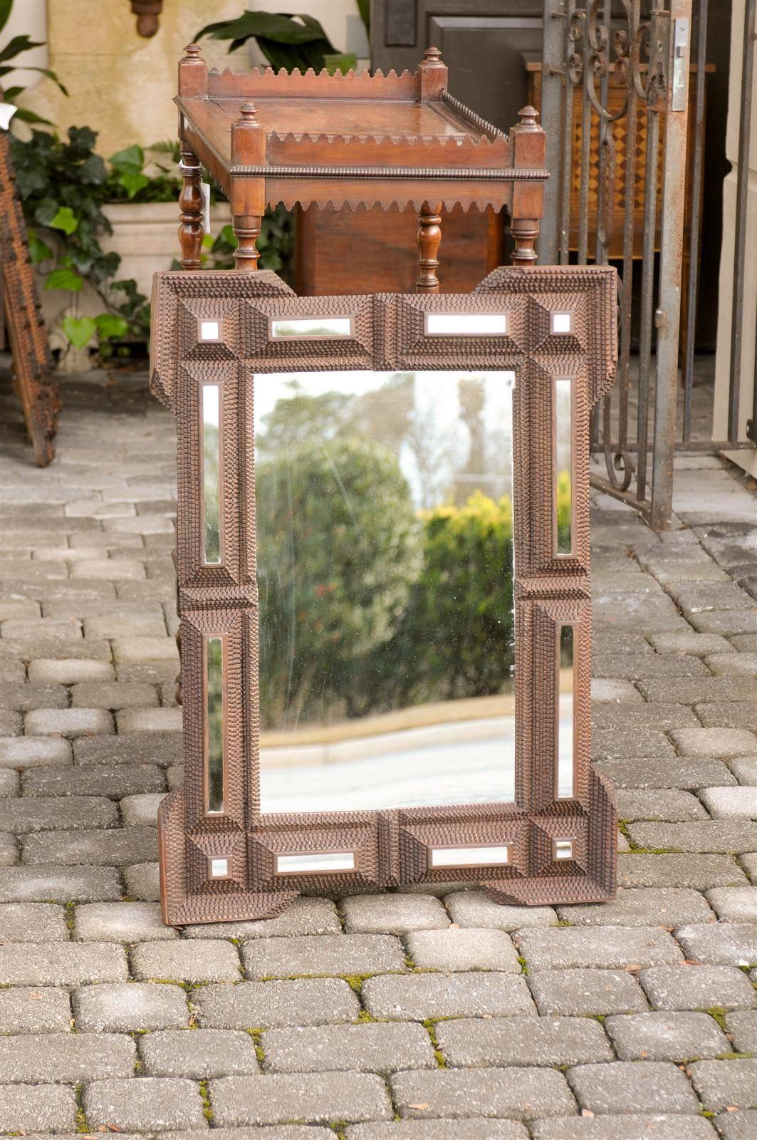 This French tramp art mirror from the turn of the century (19th to 20th) features a typically texturized frame, made of various geometrically raised panels set with mirrored parts. Each corner is doubled with an additional molding, giving an