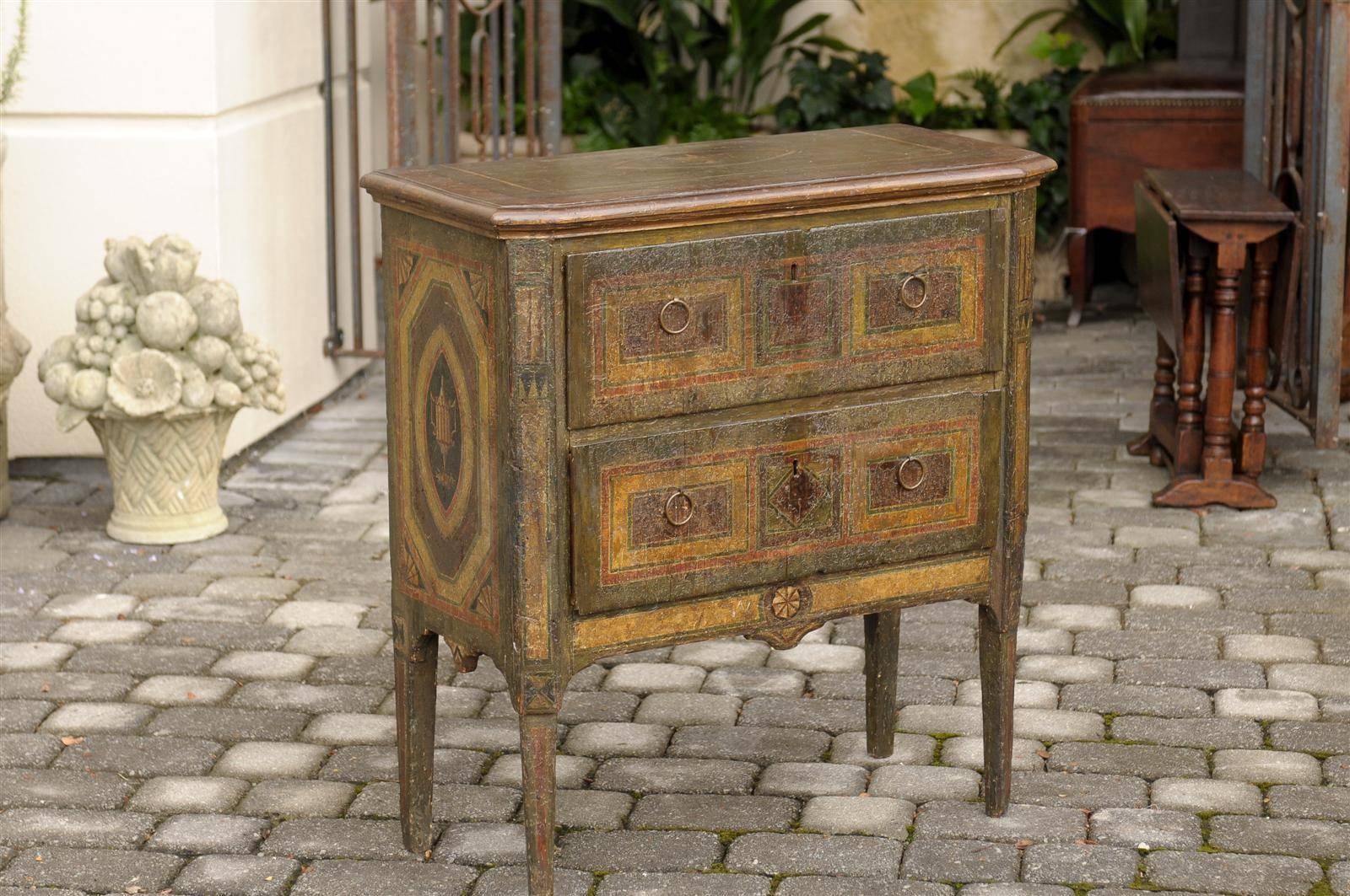 This Italian small painted commode from the very early 19th century features a rectangular top with angled front sides over two drawers. The green and brown top is decorated with a painted urn motif in the center. The exquisite sides echo this urn