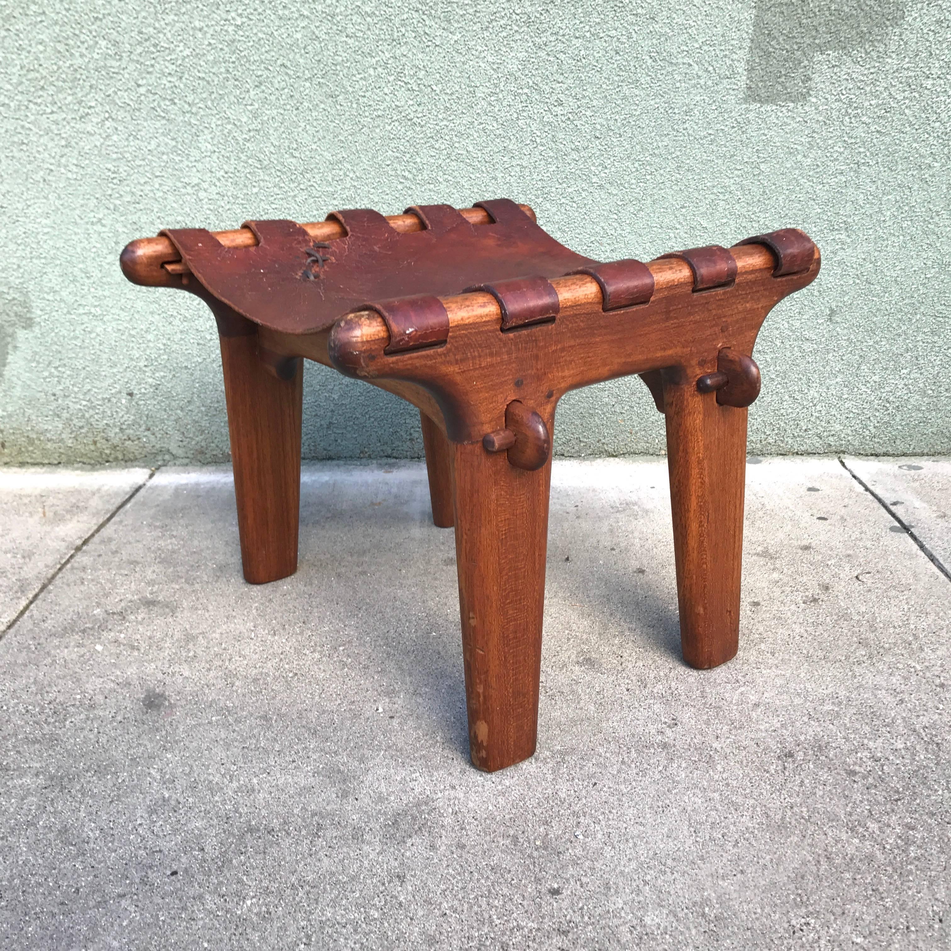 Rustic modern foot stool by Ecuadorian Angel Pazmino for Muebbles de Estillo. Constructed from mahogany and leather using peg construction for the joinery and a leather sling cover attached via wooden pegs. All original condition with age