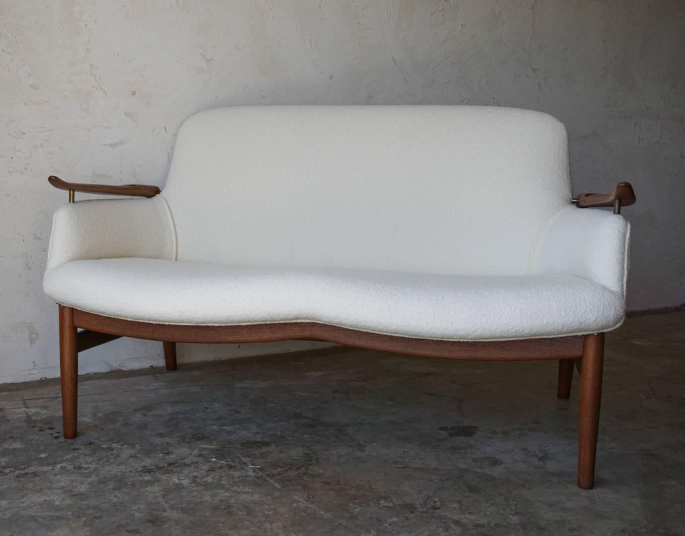 Rare NV53 settee designed by Finn Juhl for Niels Vodder, circa 1950s. Beautiful sculpted teak arms with brass details, newly restored in a pearl-colored Knoll bouclé fabric.