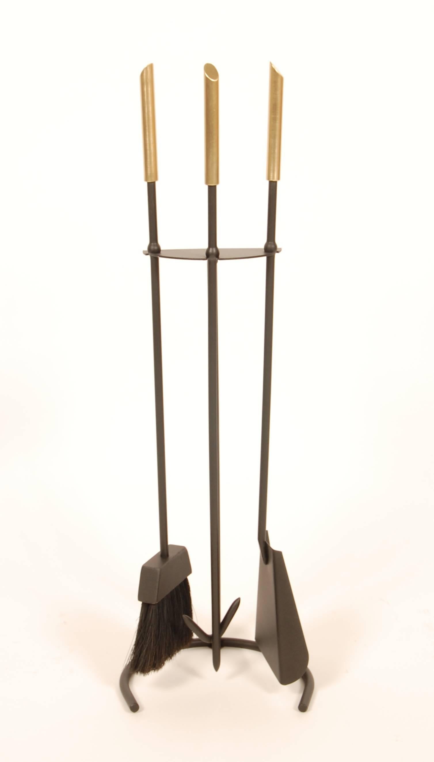 1950s modernist fire tools with a painted round stock wrought iron frame and polished brass handles. The solid brass cylindrical handles have a 45 degree taper at their ends and the iron frame has a half circle form base and utensil holder. These