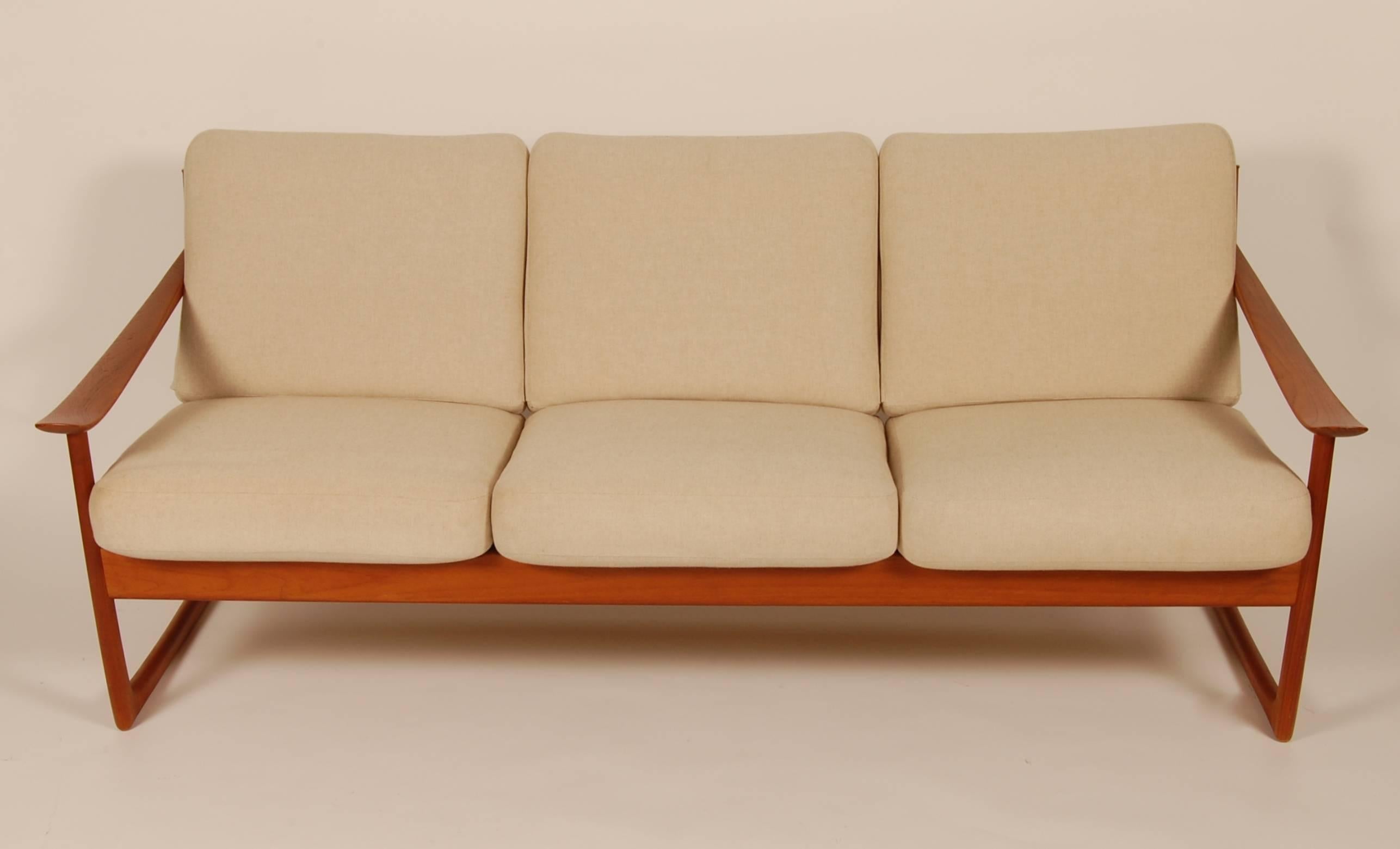 Three-seat sofa by architects Peter Hvidt and Orla Mølgaard, Nielsen, crafted by France and Son and imported for John Stuart Inc, New York, circa 1950s. The solid teak frame has a sled appearance, the back has cut a ways for the cushions to create a