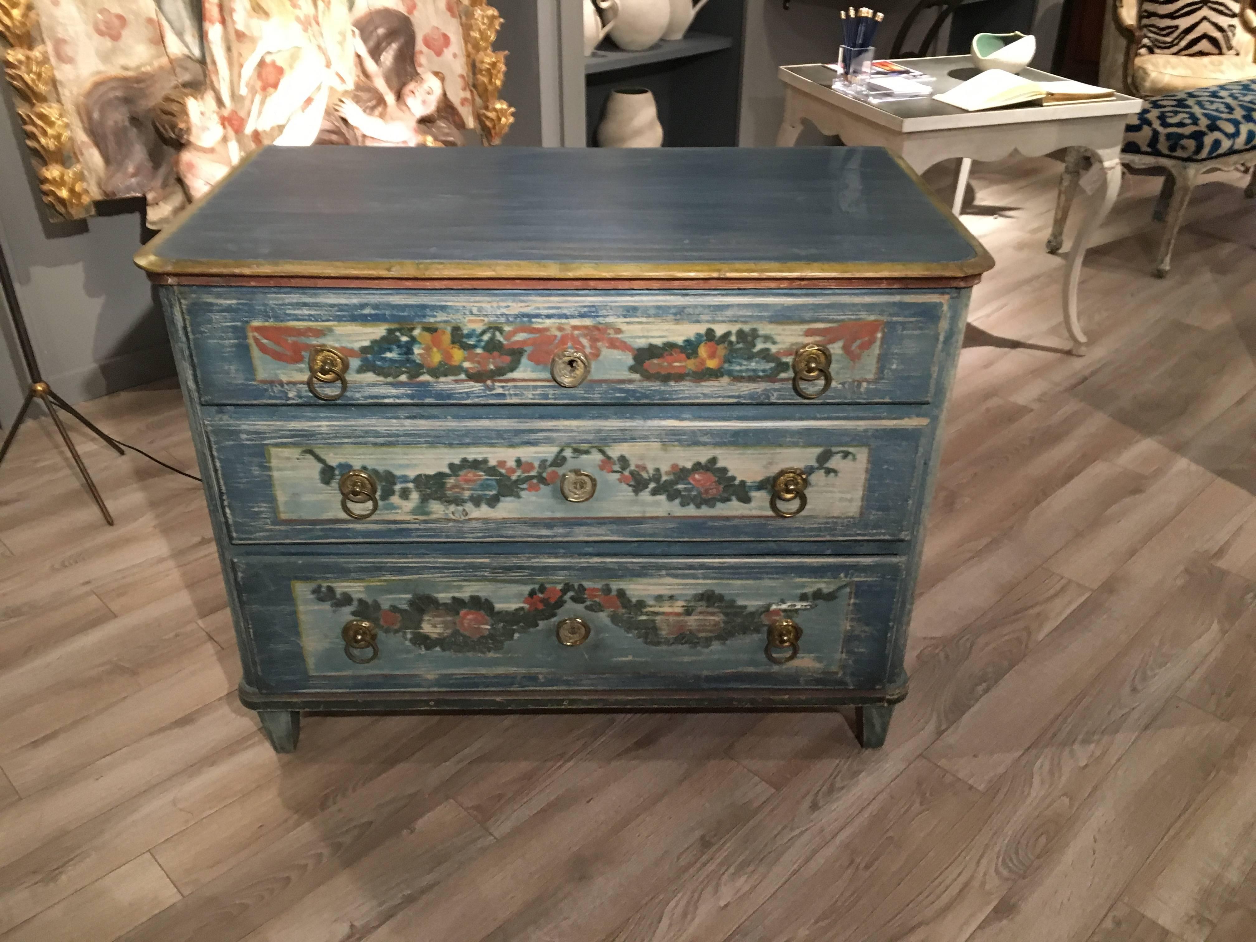 A charming three-drawer commode in pine, German or Austrian, circa 1840, retaining its original blue and cream painted finish, with decorative painted flowers, fruit and garlands, original brass drawer pulls and escutcheons.