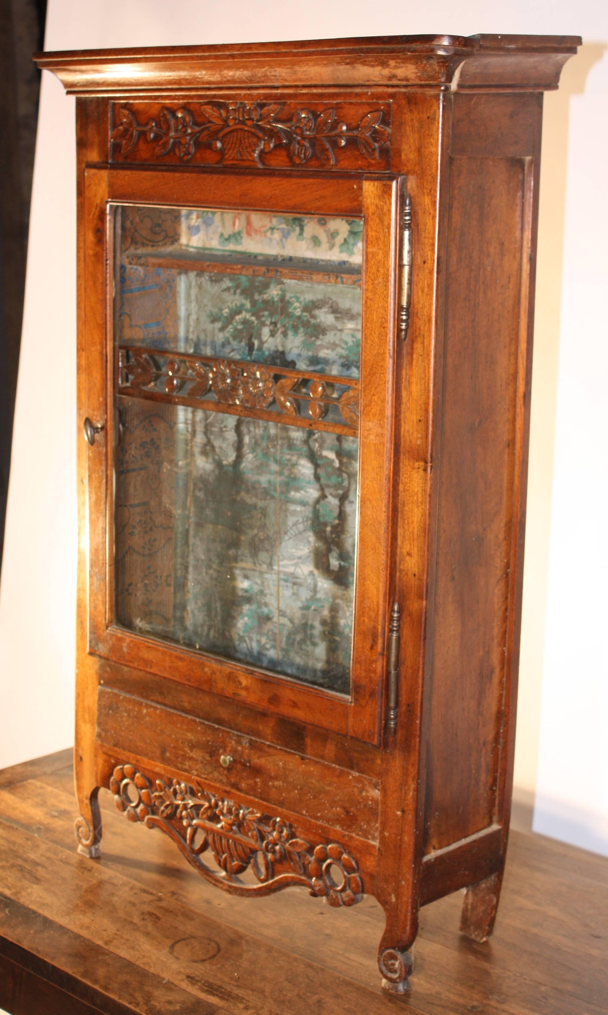 A great example of 18th century French furniture from Arles, this petite wall-hanging "verriere" is in the form of a miniature armoire in cherrywood, circa 1760, with a carved and pierced apron typical of the region. The interior is lined