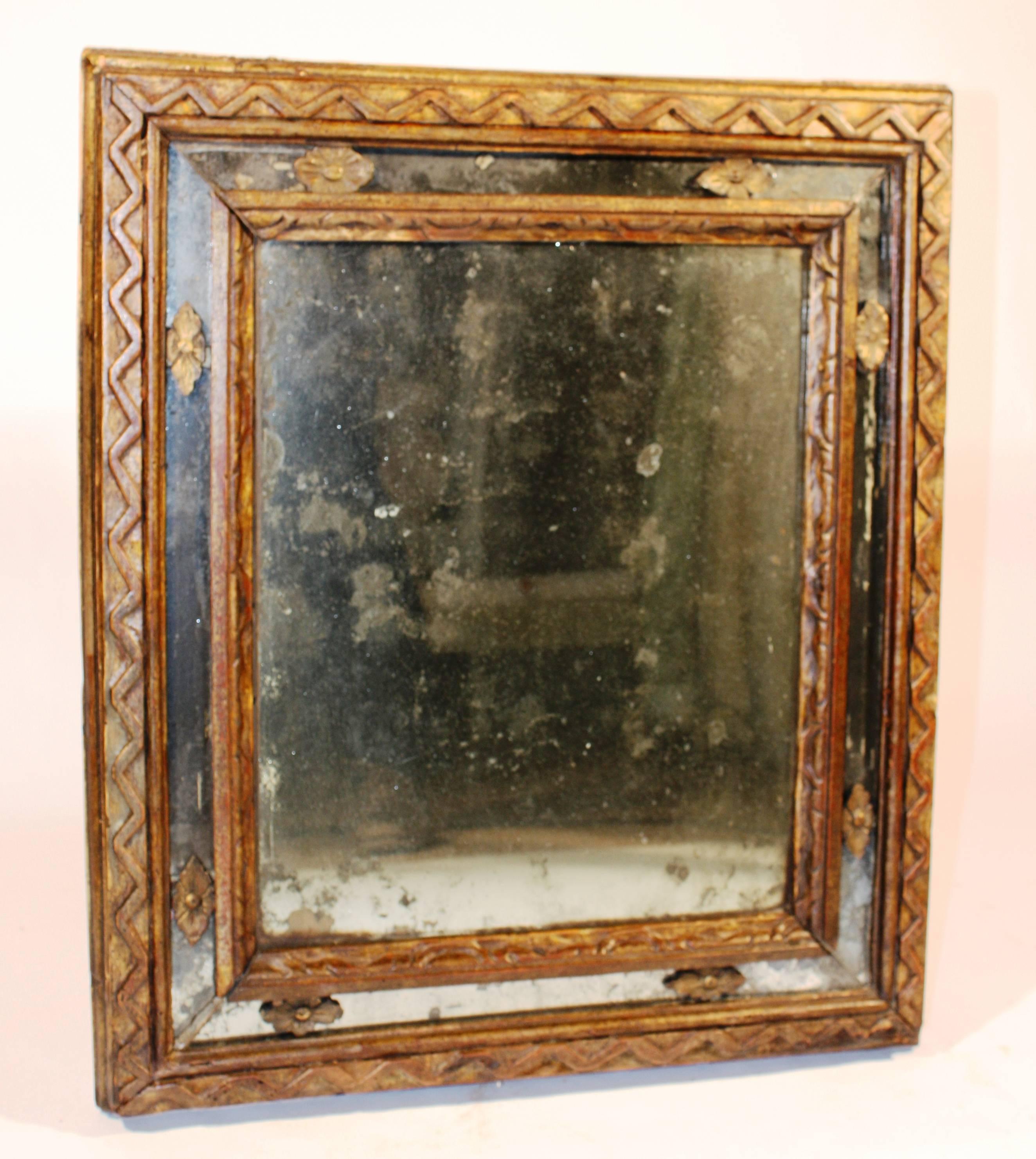 A charming 17th century Italian mirror with a giltwood frame and inset mirror panels with gilt rosettes. The gold leaf has worn through to expose the reddish brown 