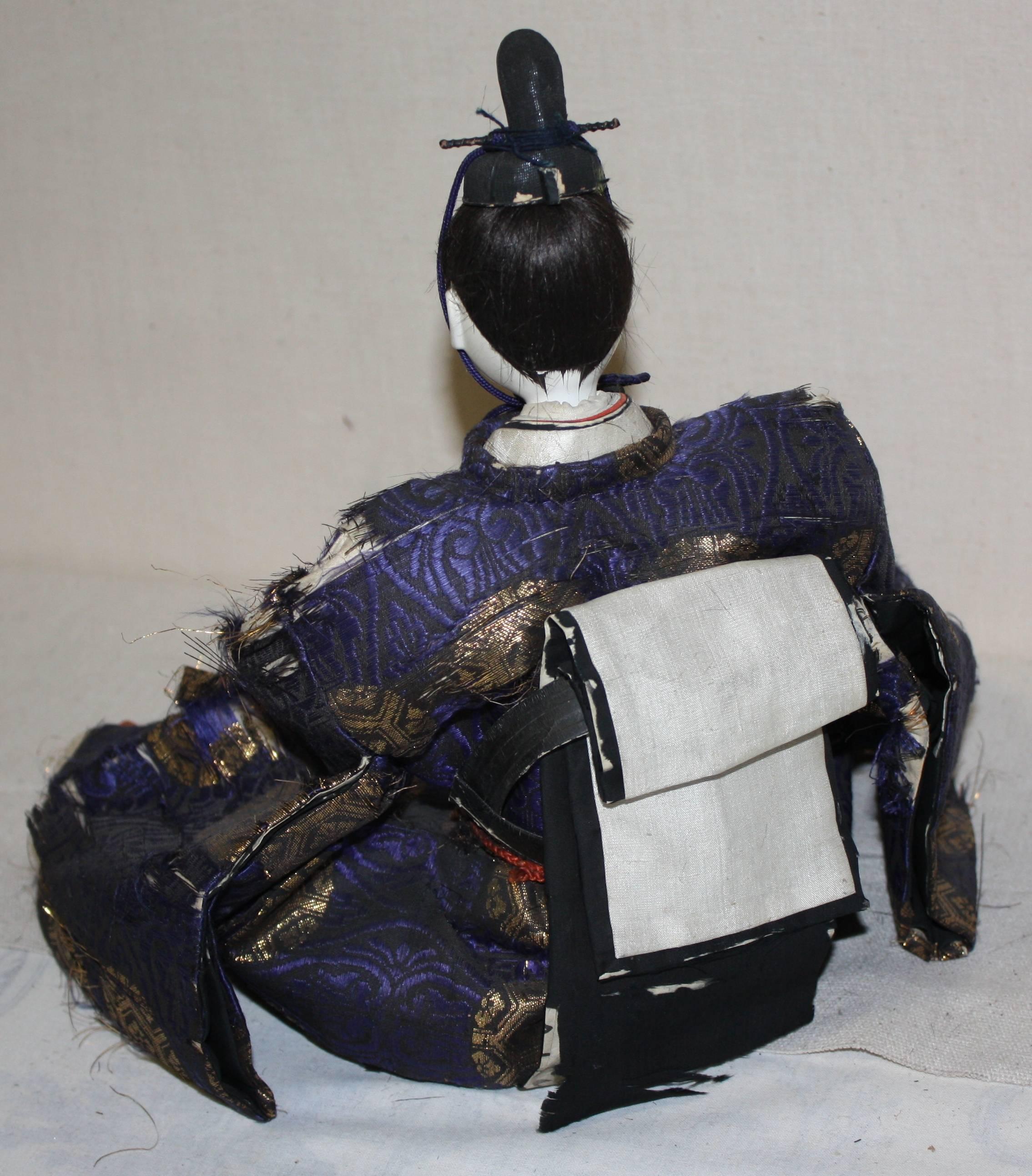 A Japanese Meiji period doll of the Emperor, with porcelain face and hands, glazed in ground oyster shells (Gofun), and wearing period costume.